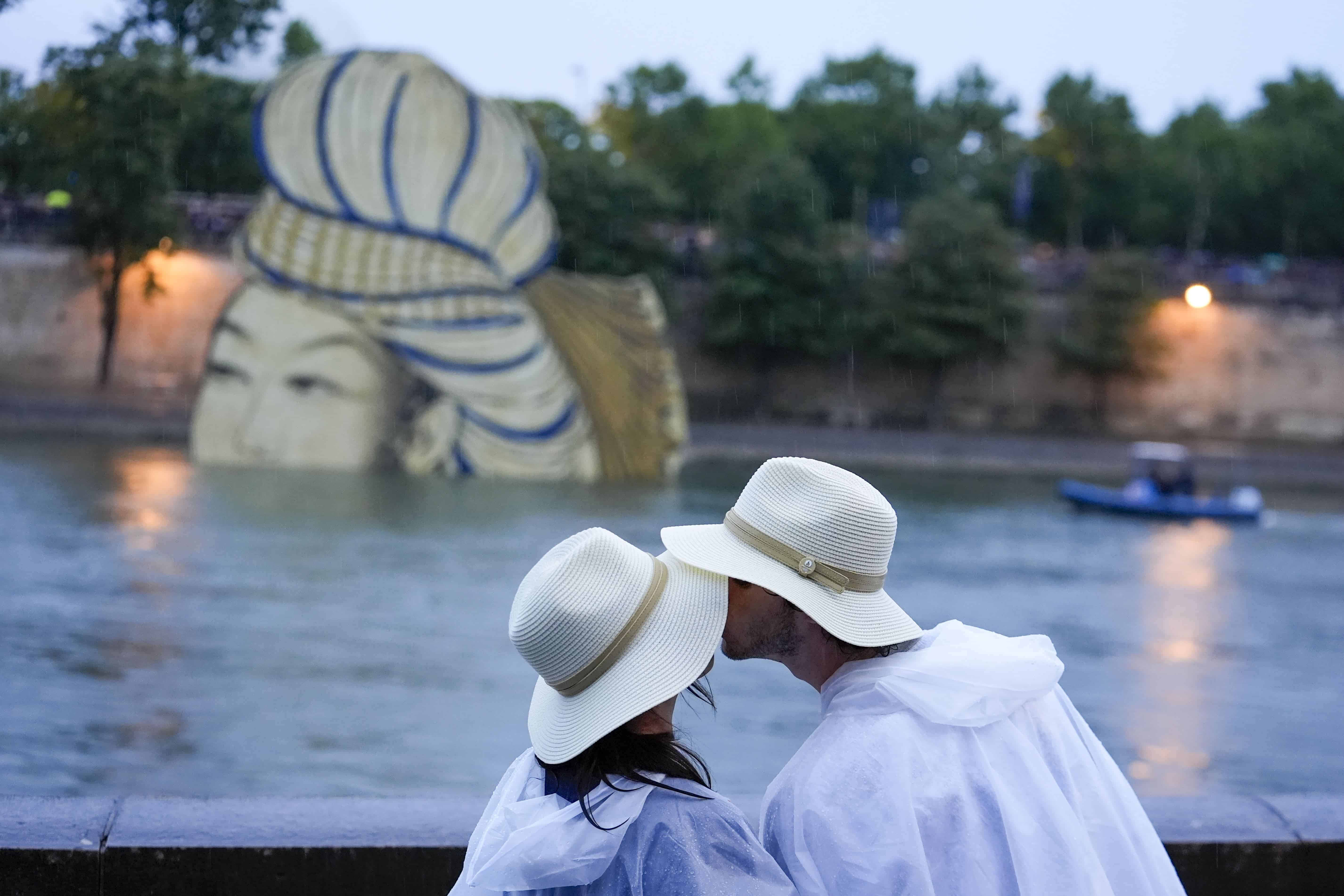 Una pareja se besa mientras espera que los barcos del equipo pasen por el Sena en París, Francia, durante la ceremonia de apertura de los Juegos Olímpicos de Verano de 2024, el viernes 26 de julio de 2024.