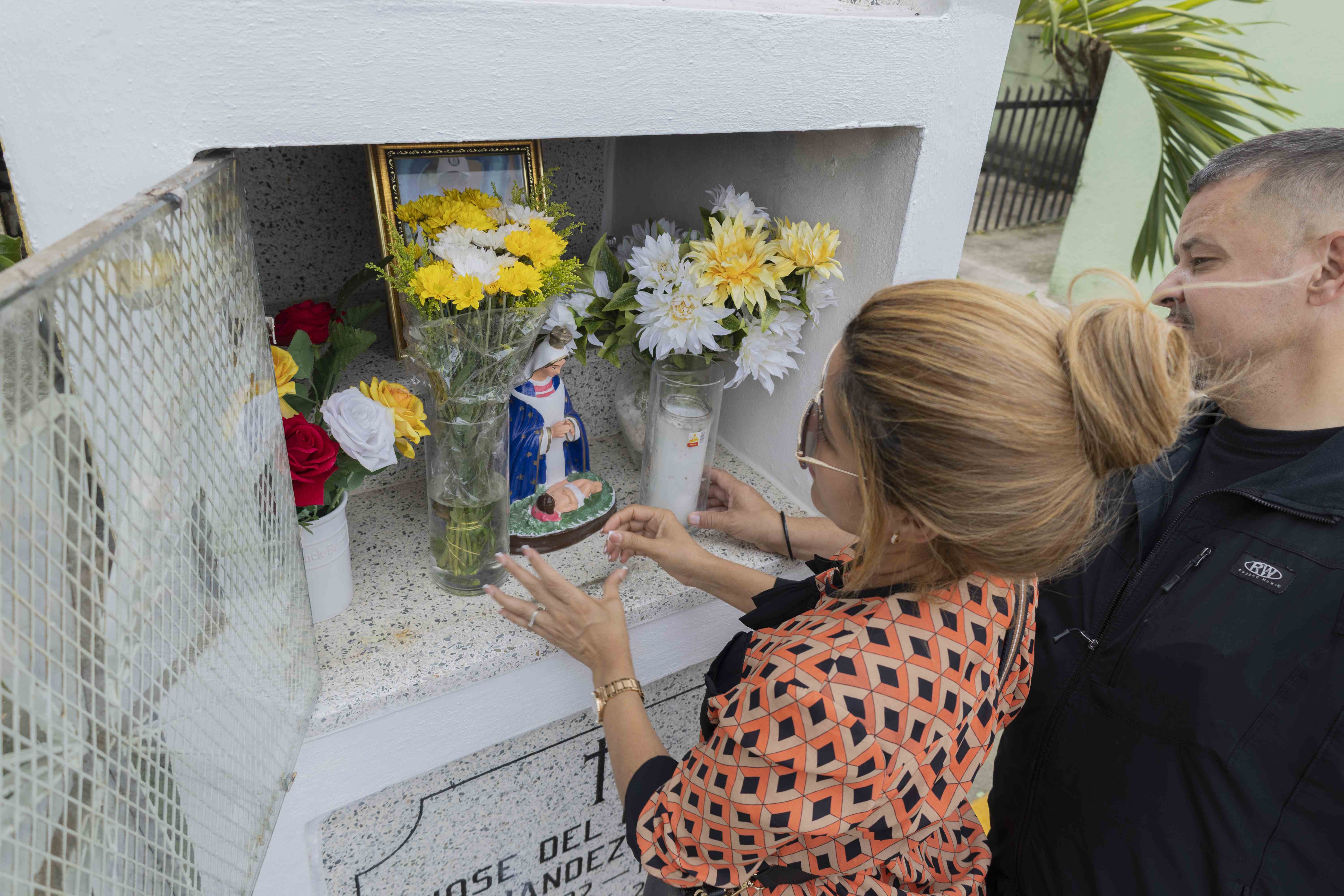 Yolanda Fernández y su esposo colocan flores y velones a la tumba de su padre, José del Carmen Fernández.