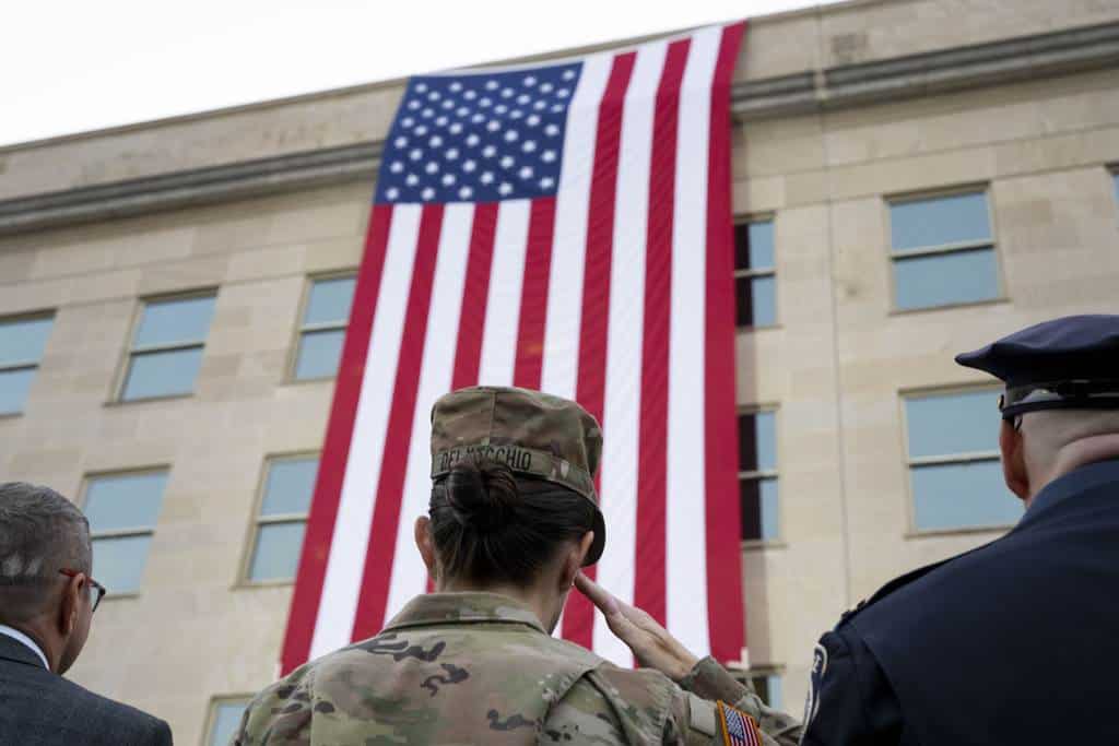 Miembros del ejército y socorristas saludan mientras se despliega una bandera desde lo alto del Pentágono durante una ceremonia conmemorativa del 11 de septiembre al amanecer el miércoles 11 de septiembre de 2024 en Washington.