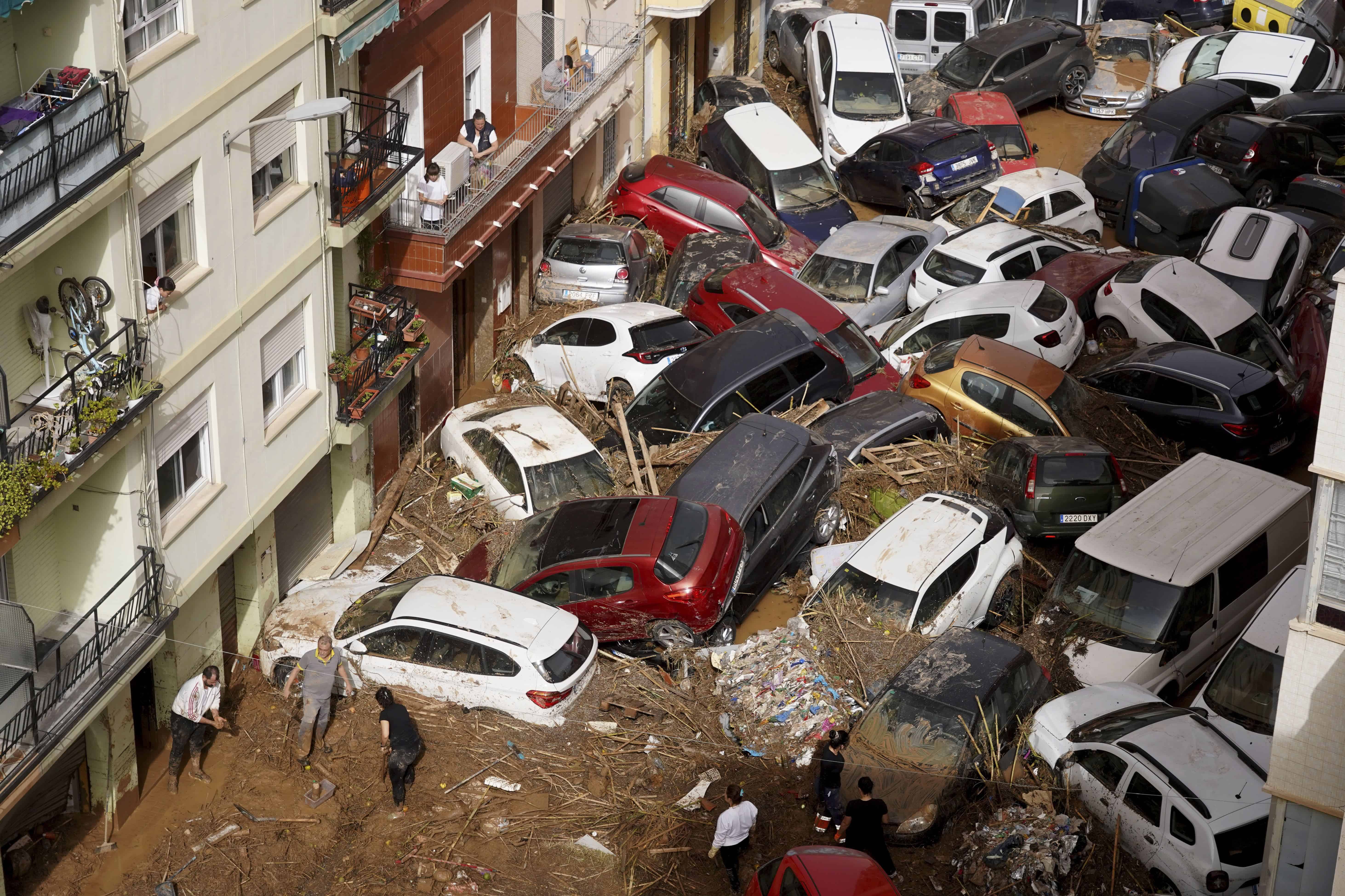 Los residentes limpian la calle junto a los autos amontonados después de ser arrastrados por las inundaciones en Valencia, España, el miércoles 30 de octubre de 2024.