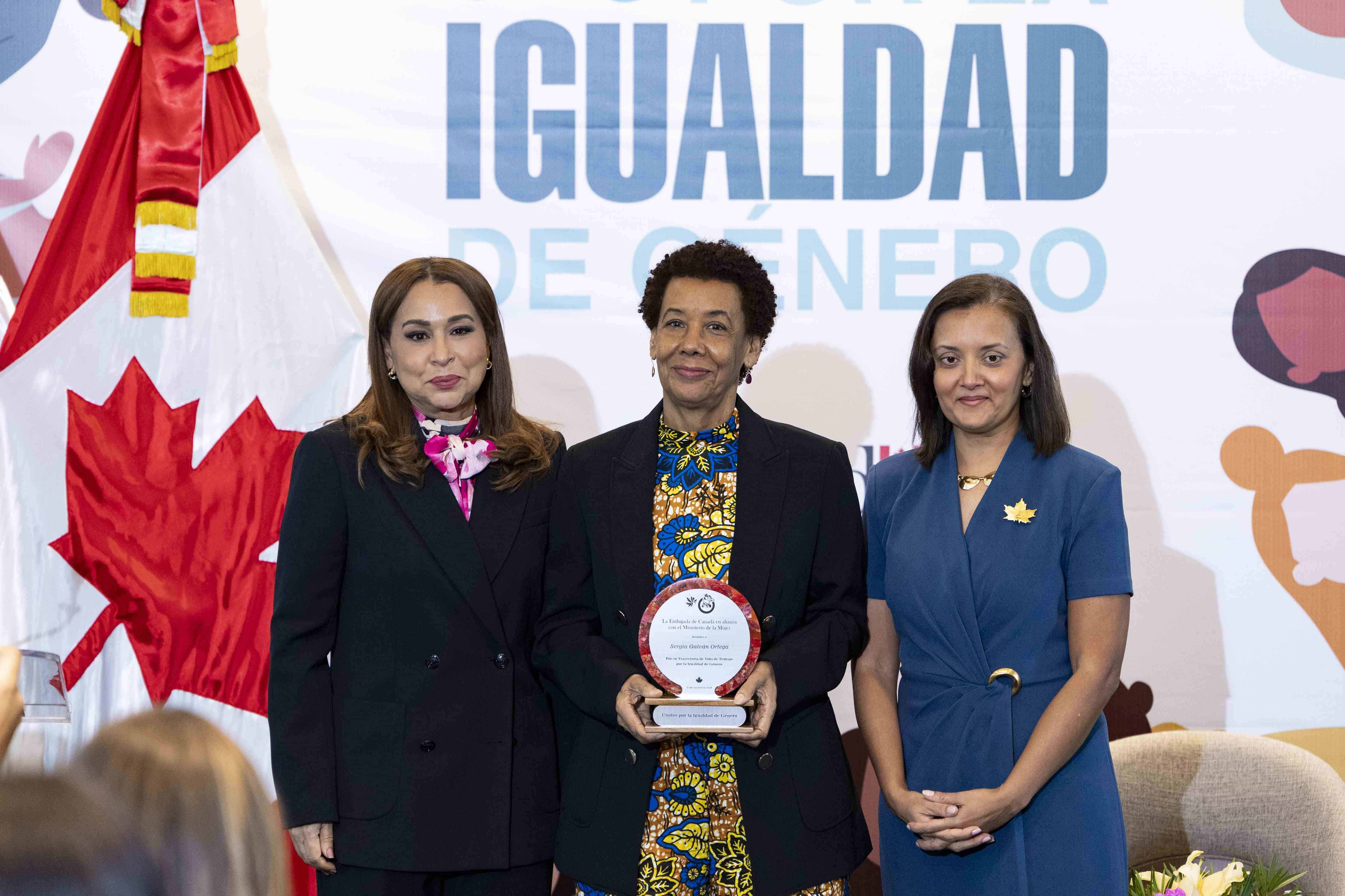 Sergia Galván recibe distinción de manos de Mayra Jiménez y Jacqueline DeLima.