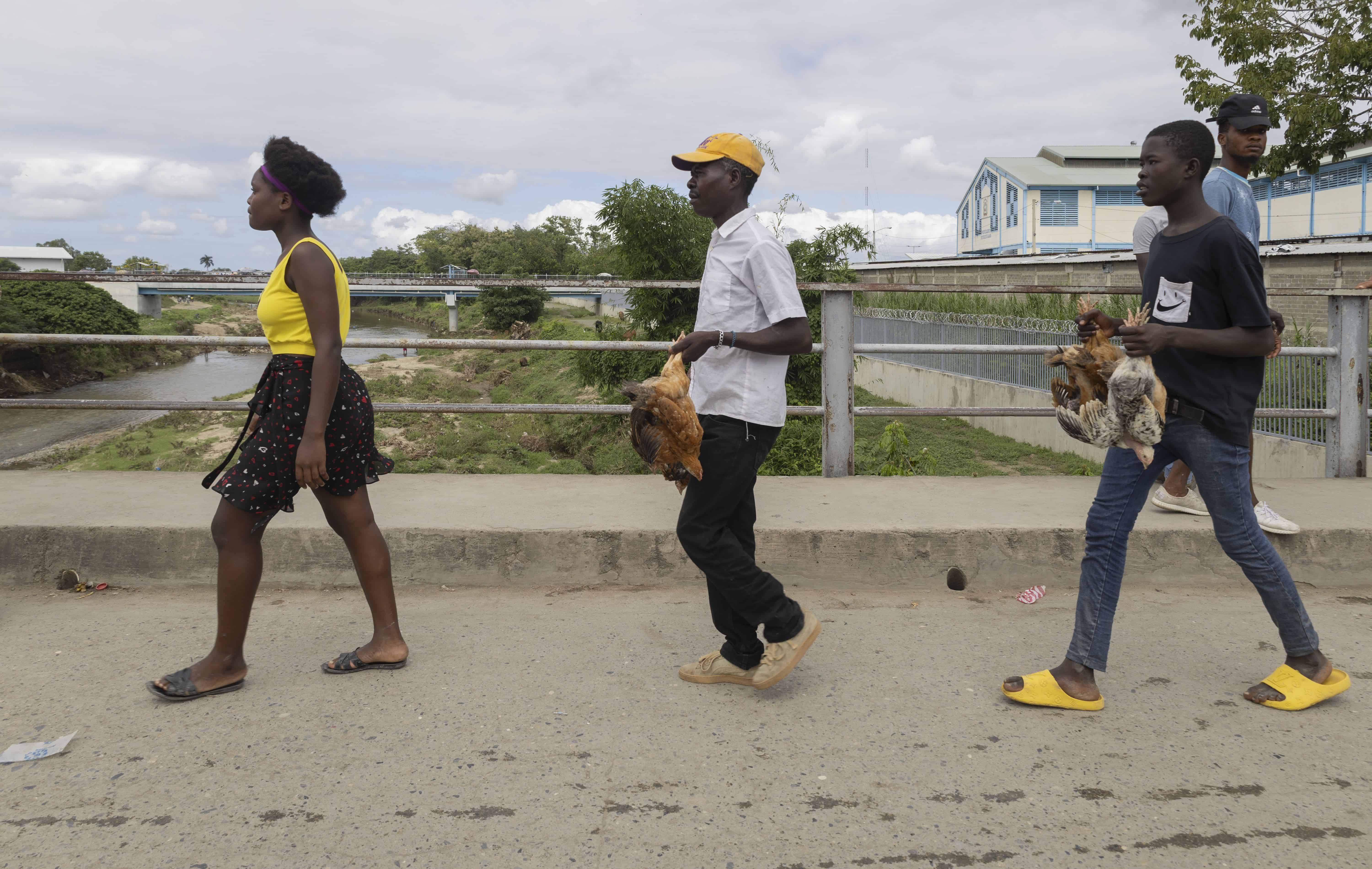 Tres haitianos, con prendas amarillas, caminan hacia Haití.