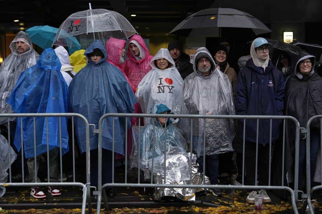 Varias personas de pie bajo la lluvia en la Sexta Avenida previo al inicio del desfile de Macy's por el Día de Acción de Gracias, el jueves 28 de noviembre de 2024, en Nueva York.