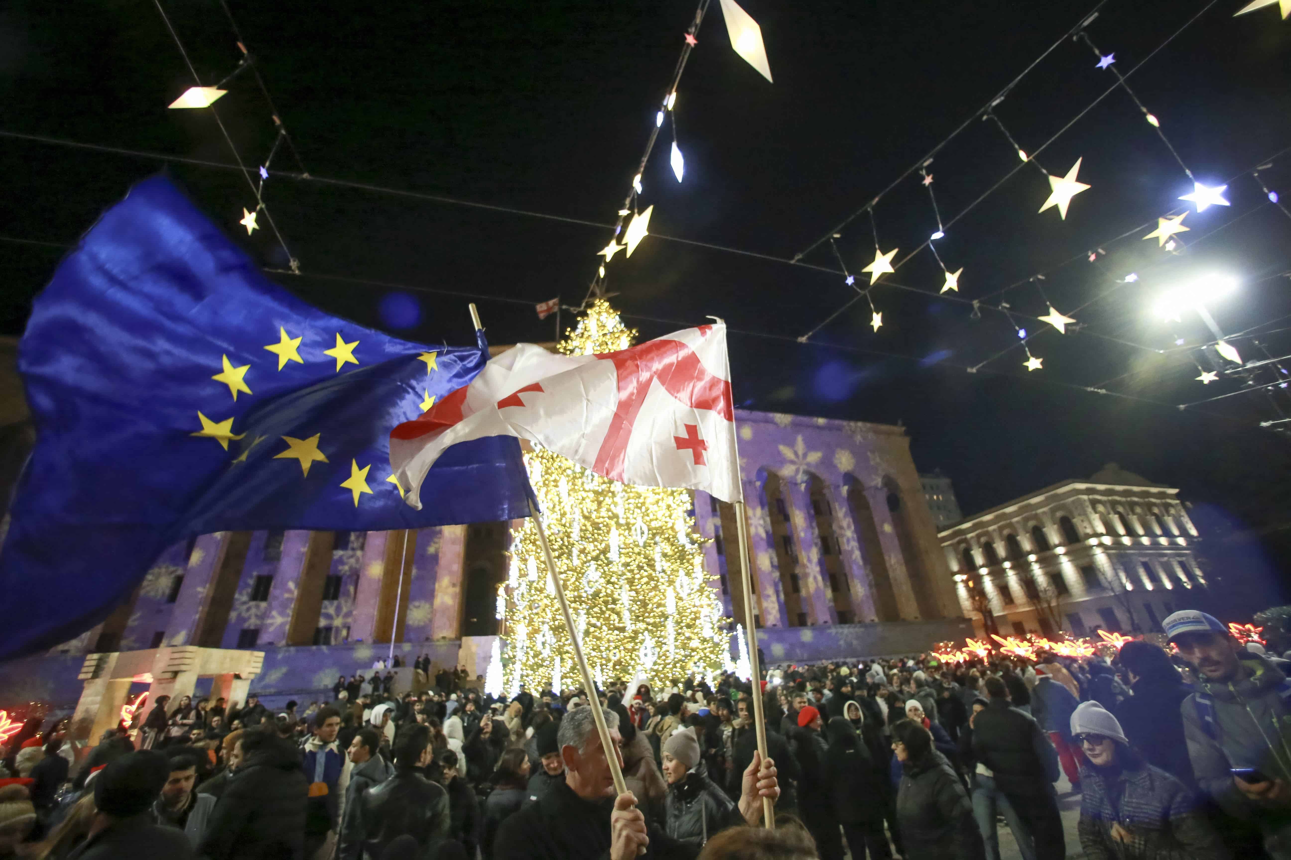 Personas con banderas nacionales y de la UE se reúnen en una calle decorada para las festividades de Navidad y Año Nuevo en la víspera de Año Nuevo fuera del parlamento georgiano, en Tbilisi, Georgia, el martes 31 de diciembre de 2024.