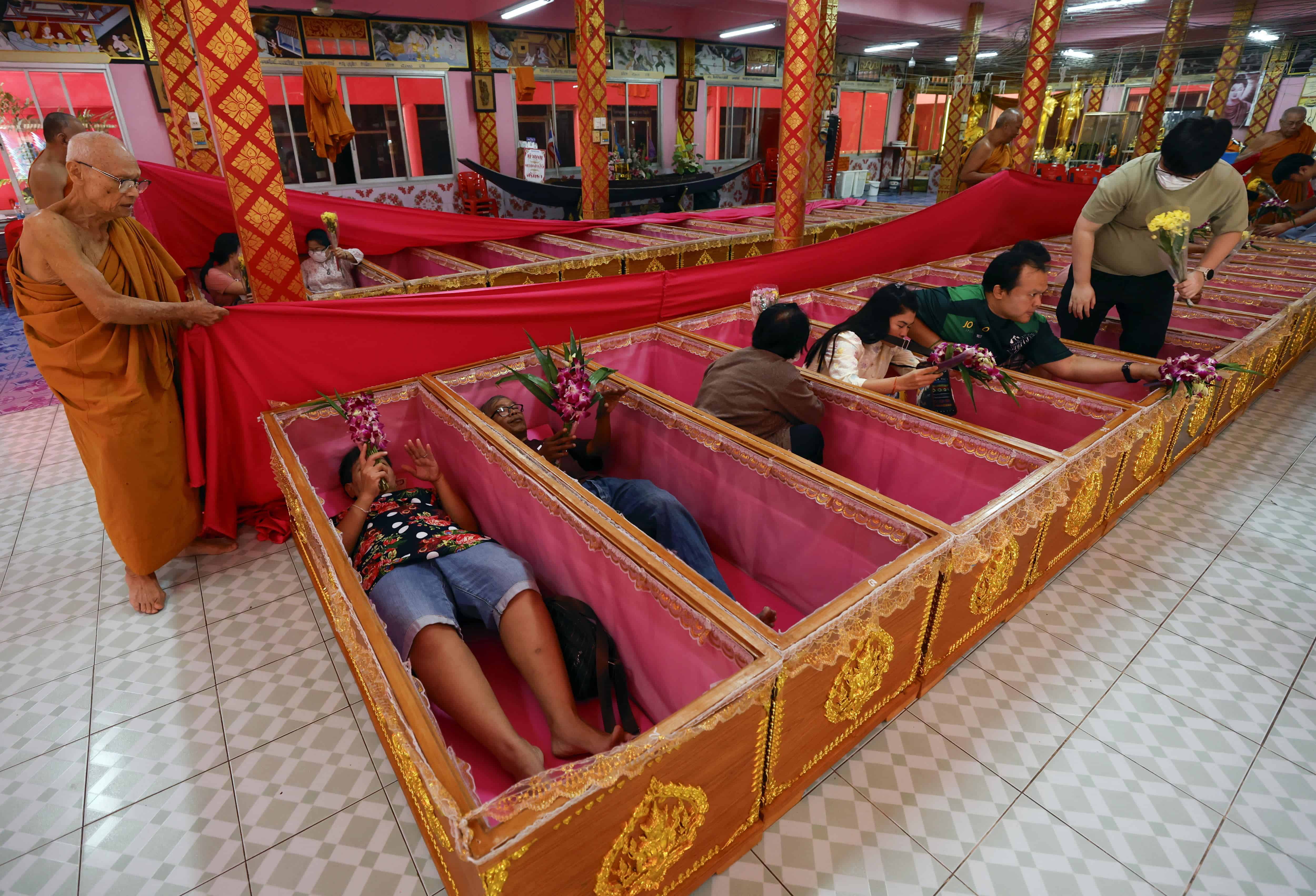 Varias personas rezan dentro de los féretros mientras un monje budista realiza el rito durante la ceremonia de la resurrección para dar la bienvenida a 2025 en el templo Wat Takien en las afueras de Bangkok, Tailandia.