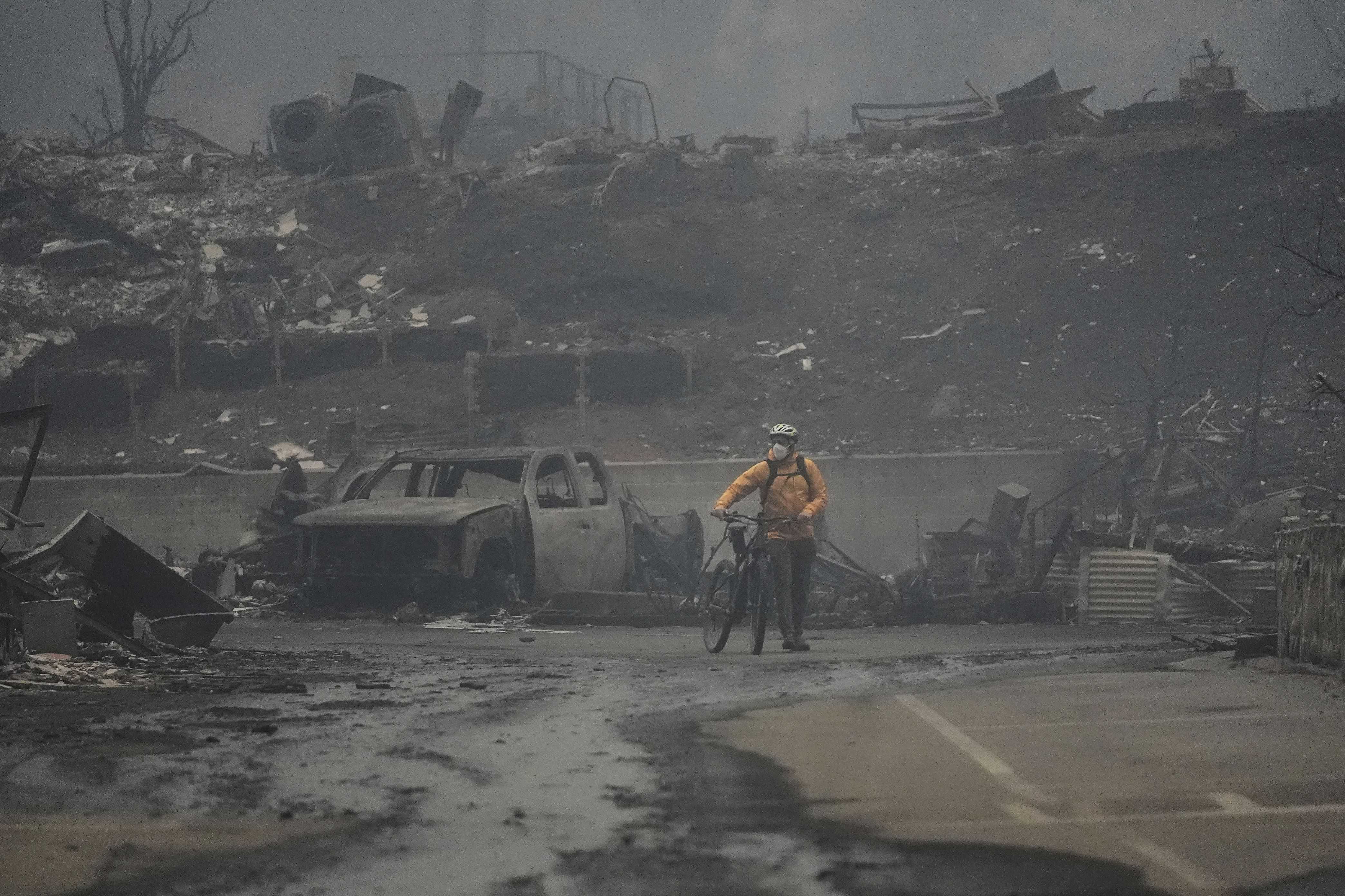 Un hombre camina en bicicleta entre las ruinas dejadas por el incendio de Palisades en el barrio Pacific Palisades de Los Ángeles, miércoles 8 de enero de 2025.