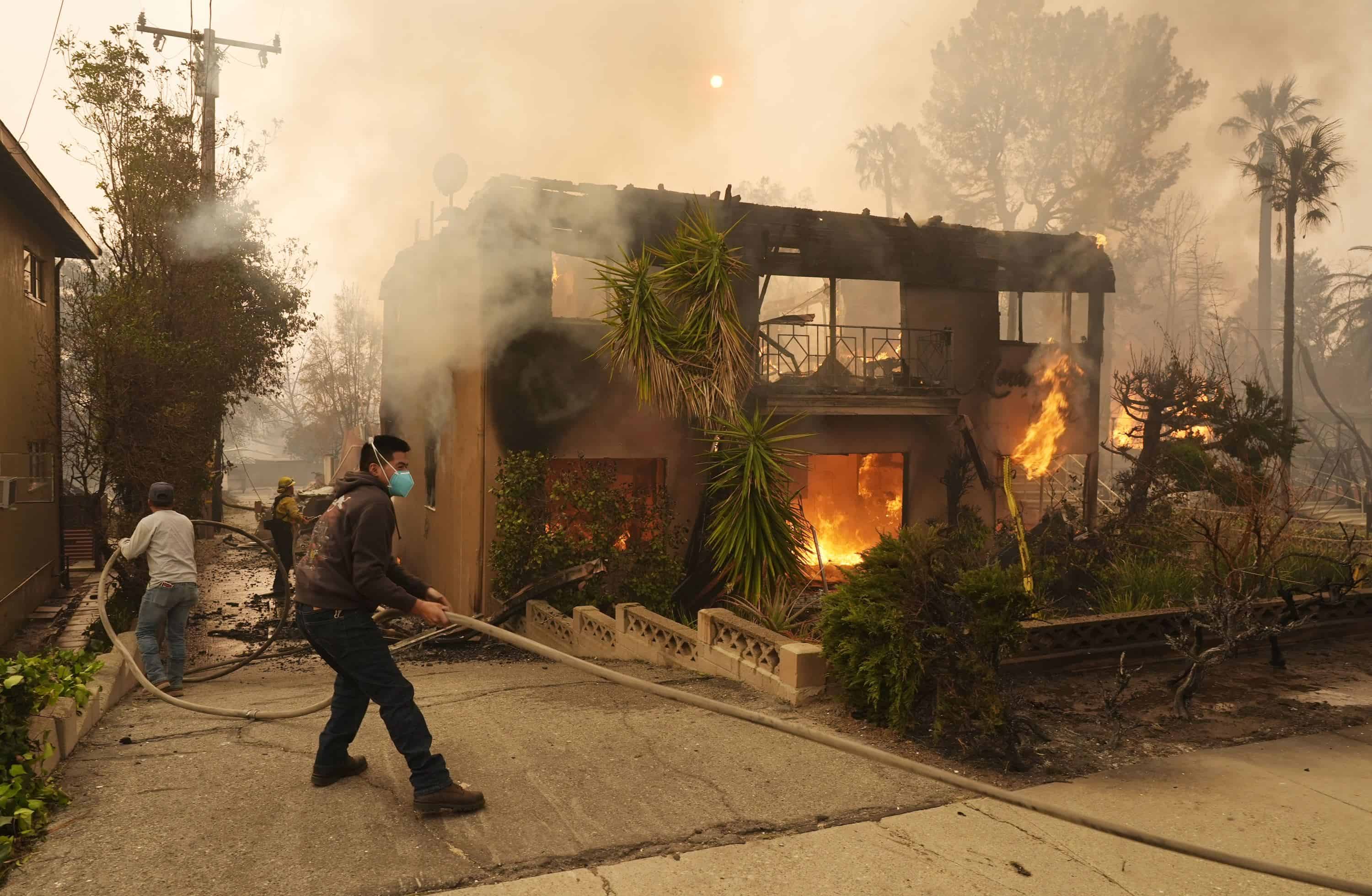 Los peatones ayudan a un bombero a estirar una manguera mientras un edificio de apartamentos se quema, el miércoles 8 de enero de 2025, en la sección Altadena de Pasadena, California.