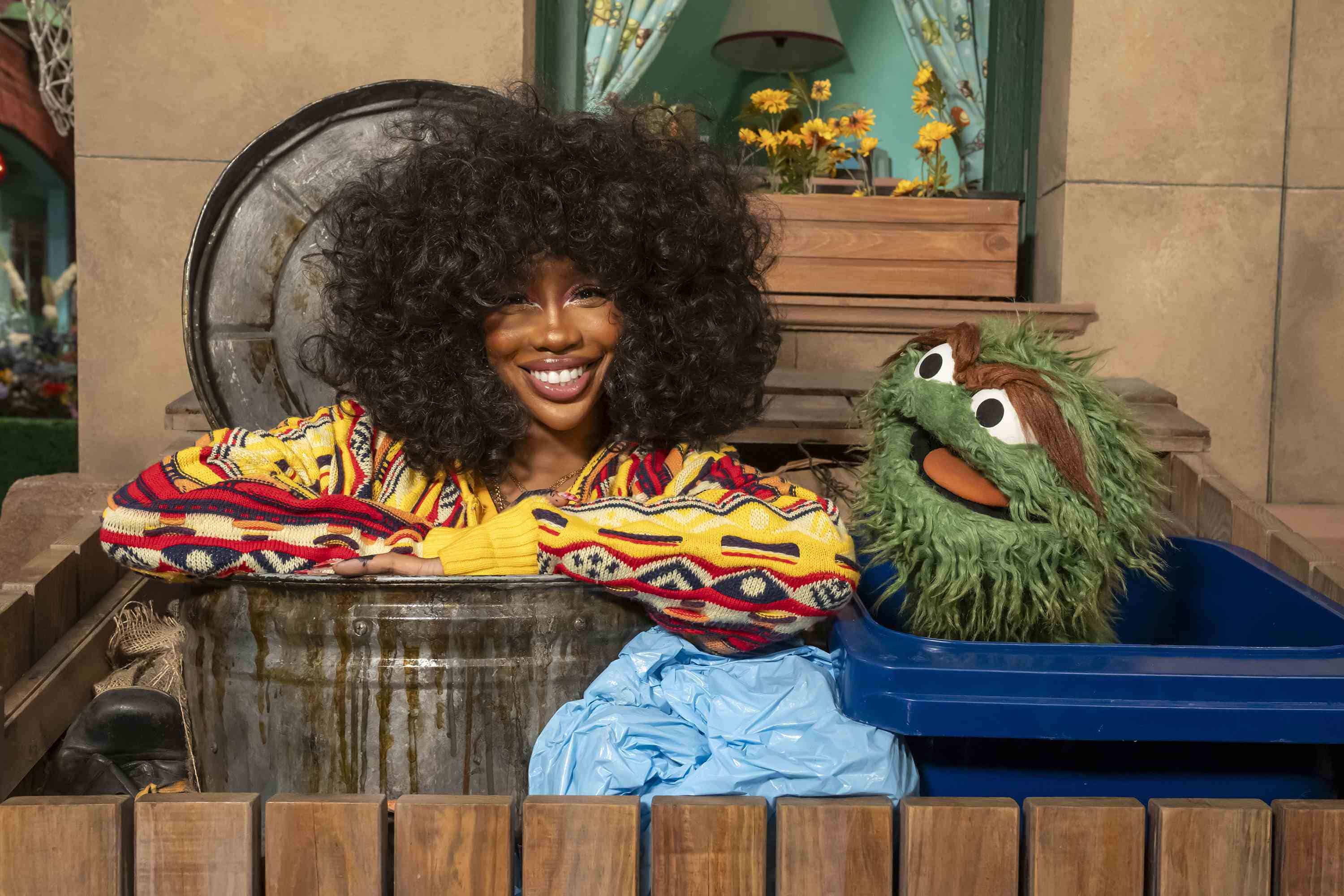 Esta imagen proporcionada por Sesame Workshop muestra al cantante SZA, a la izquierda, con el personaje de los muppets Oscar the Grouch en el set de Sesame Street. 