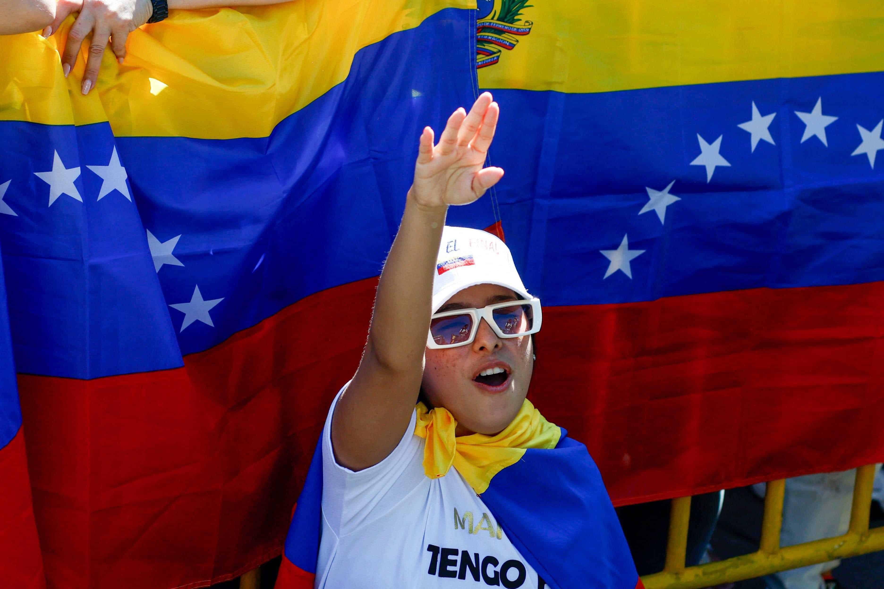 Una venezolana residente en República Dominicana levanta la mano en señal de victoria, mientras de fondo compañeros sostienen dos banderas de su país.