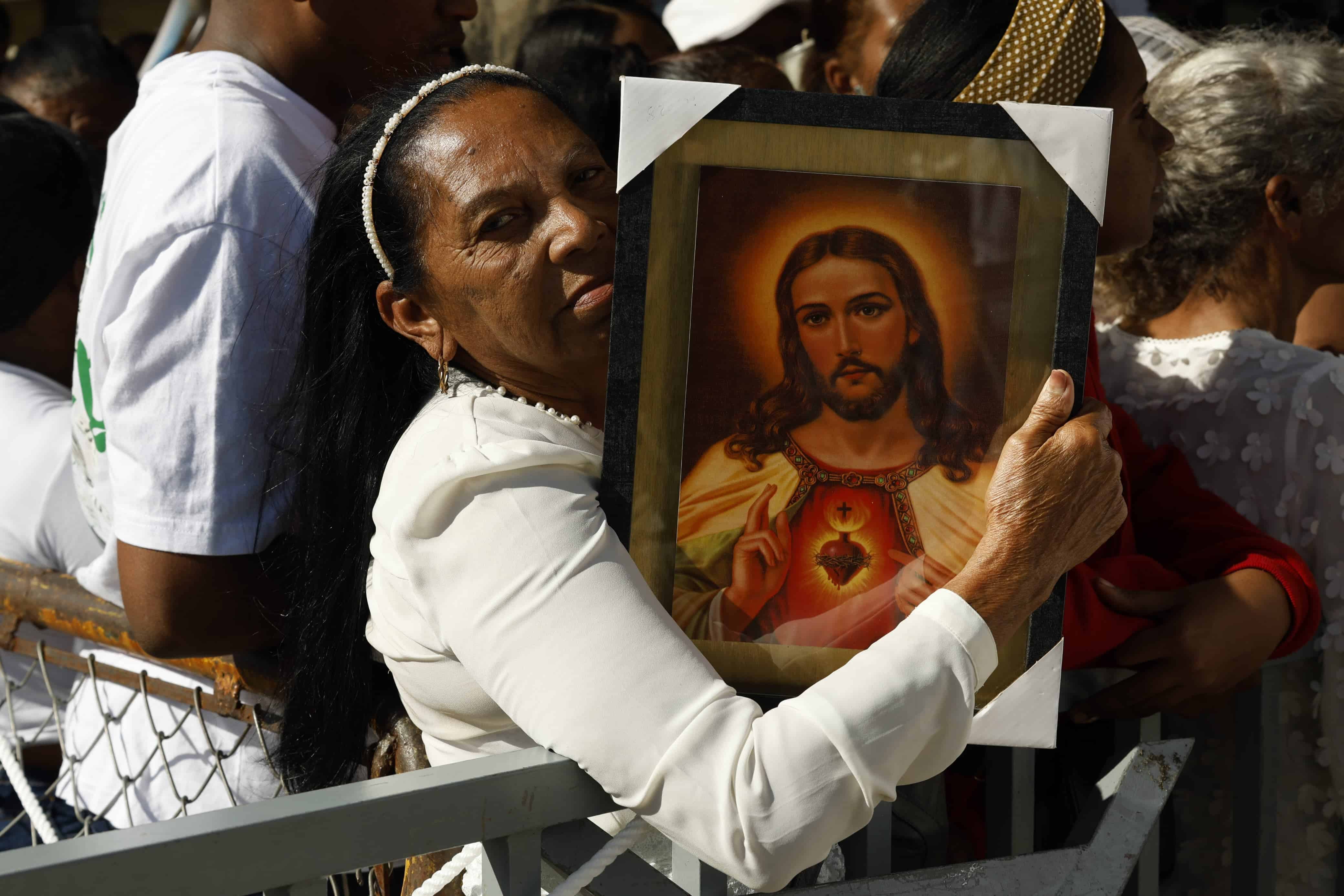 Portando una imagen del Sagrado Corazón de Jesús, una mujer espera su turno para ingresar a la Basilica de Higüey.