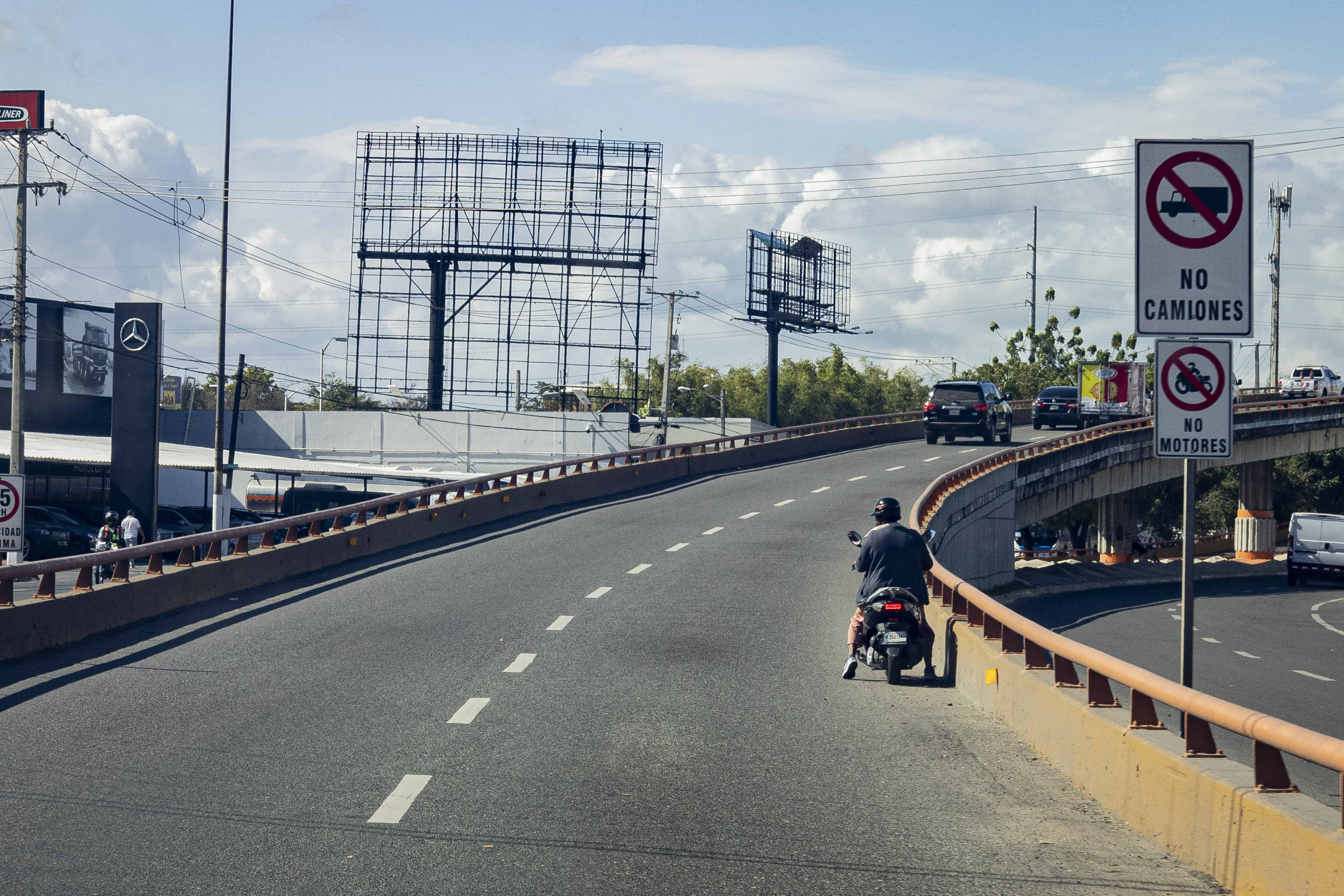 Mujer motorista, dudando al entrar al elevado.