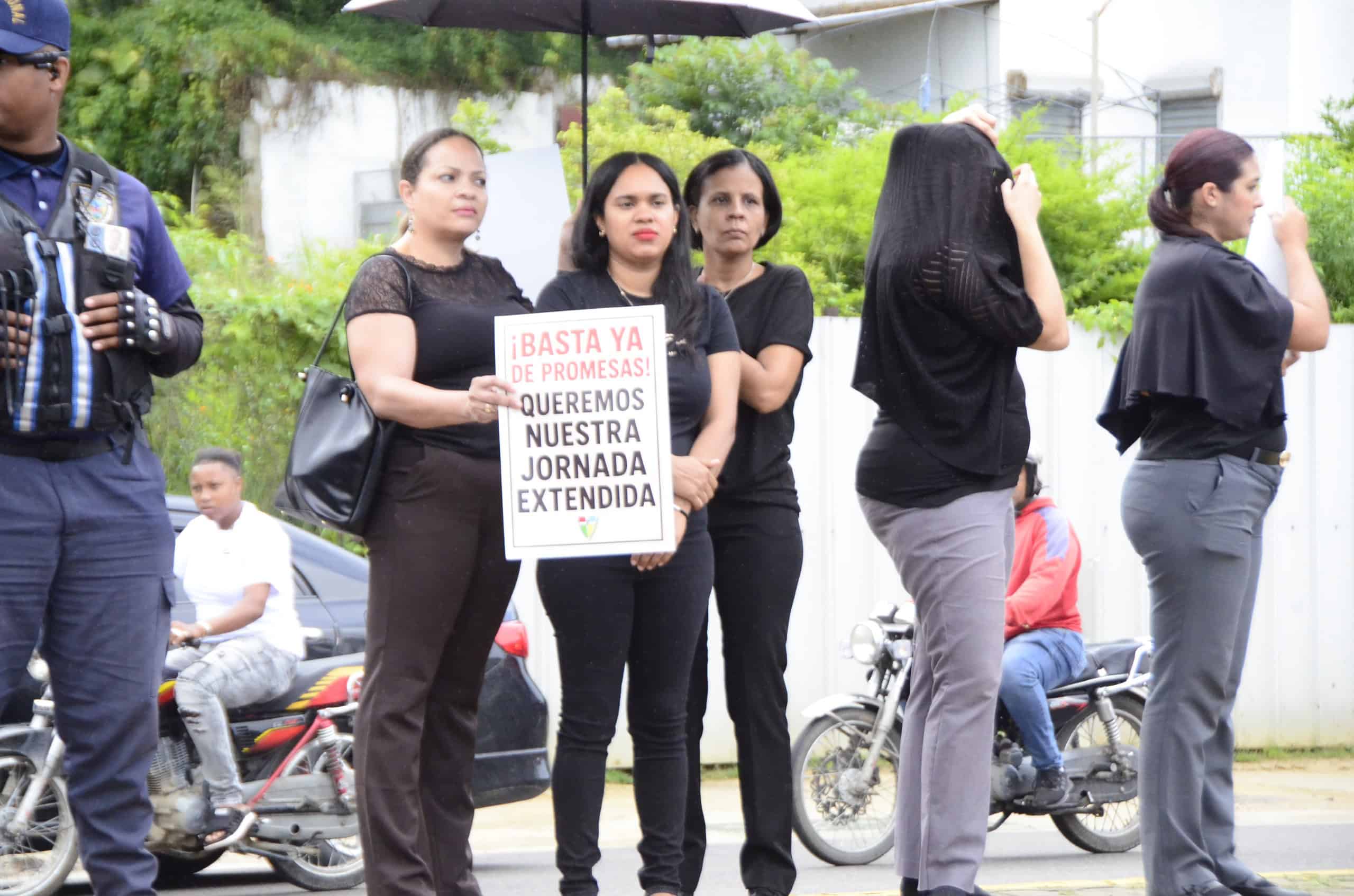 Grupo de padres y docentes vestidos de negros, exhiben pancartas en sus manos durante protesta por culminación de aulas