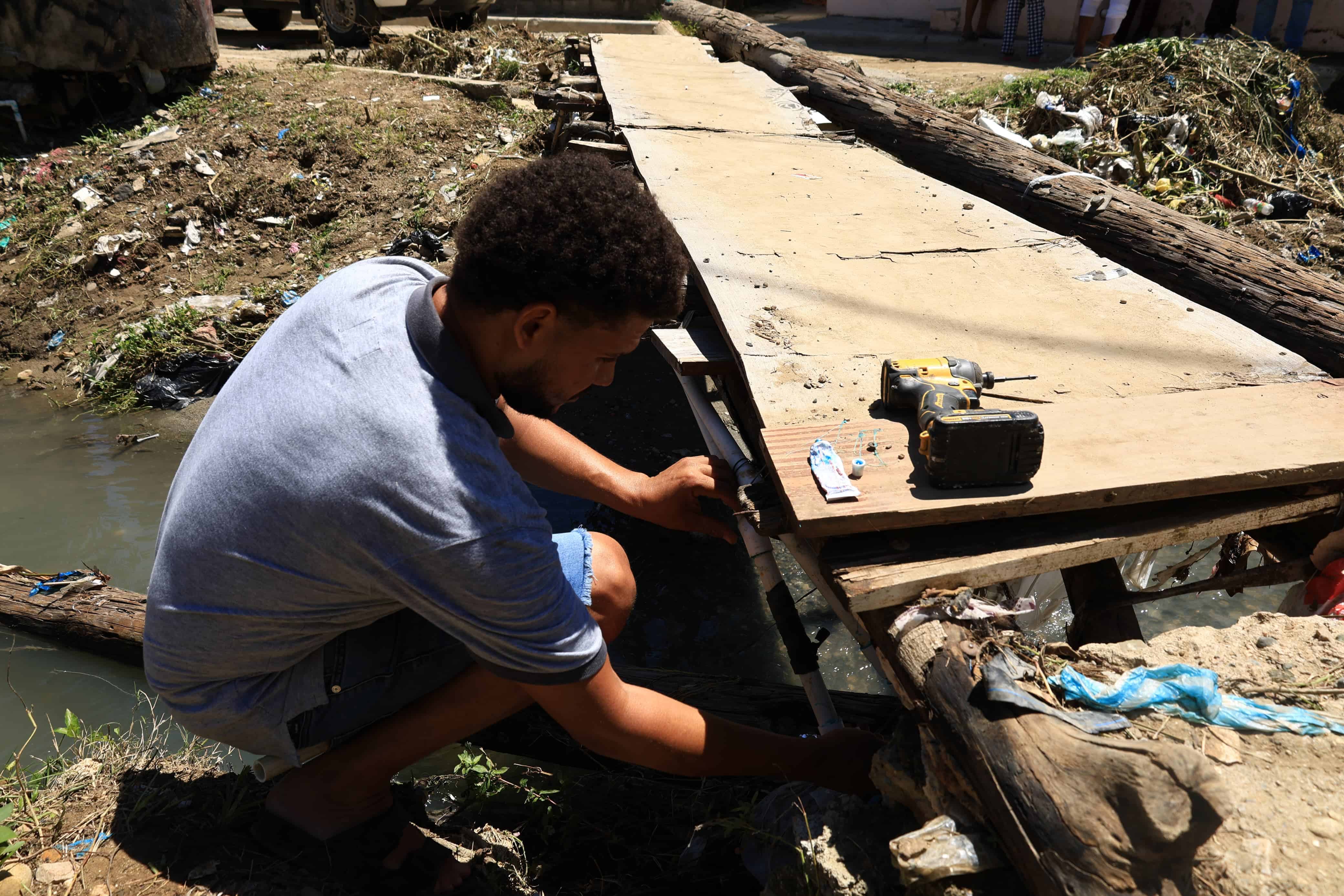 Joven repara puente improvisado sobre una cañada en la comunidad de Lavapié, provincia San Cristóbal.
