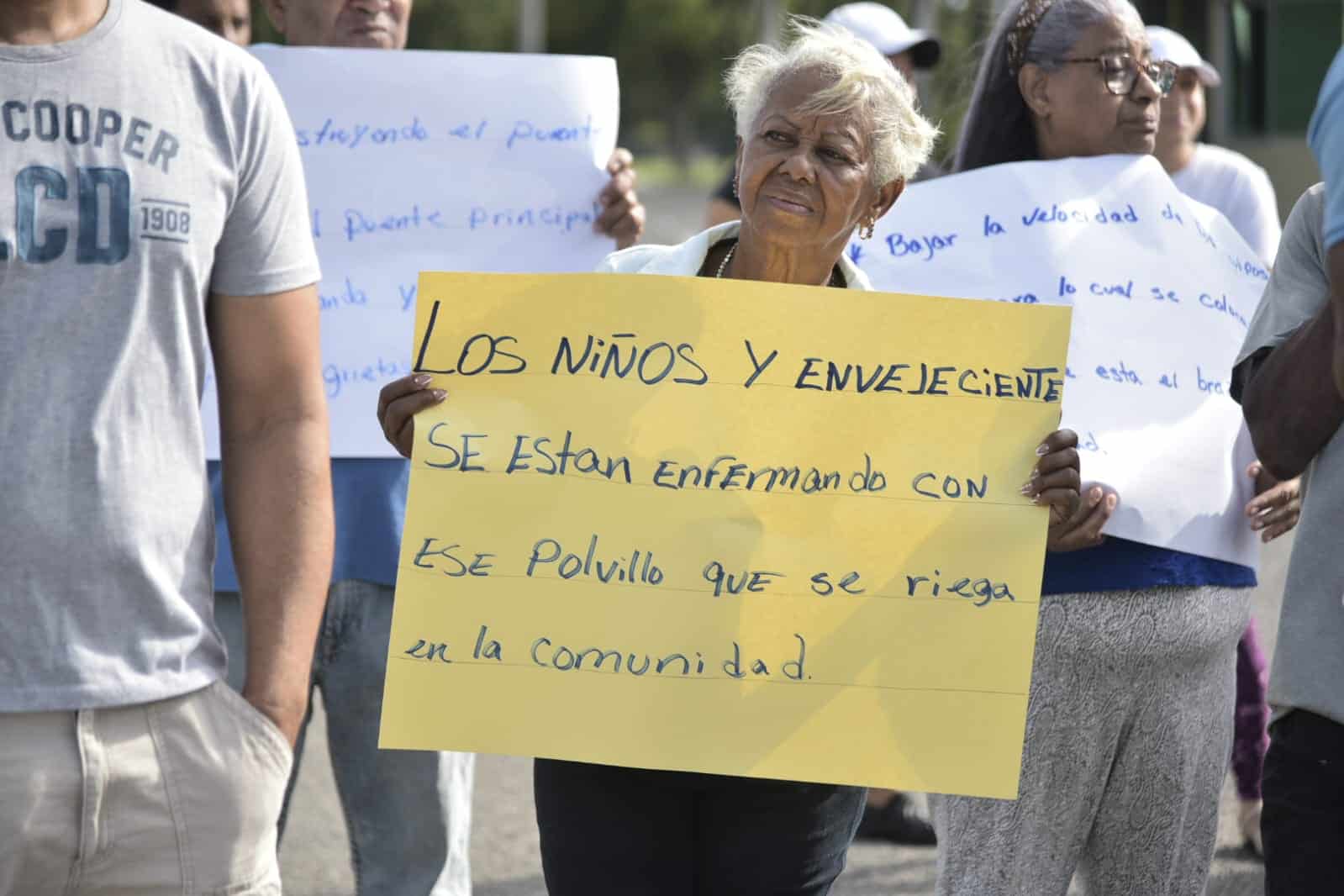 Una residente muestra un cartel en el que denuncia que niños y envejecientes están enfermando por el polvo que genera la concretera instalada en la zona, este 27 de mayo de 2025.