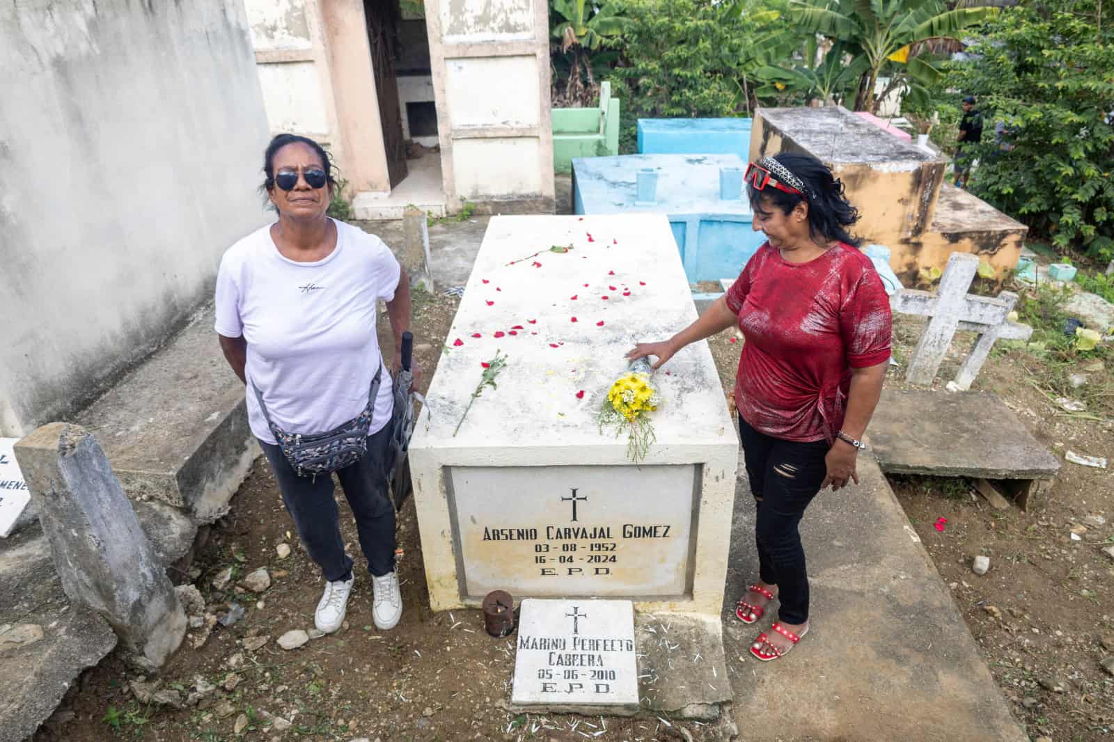 Hijas llevan flores a su padre fallecido.