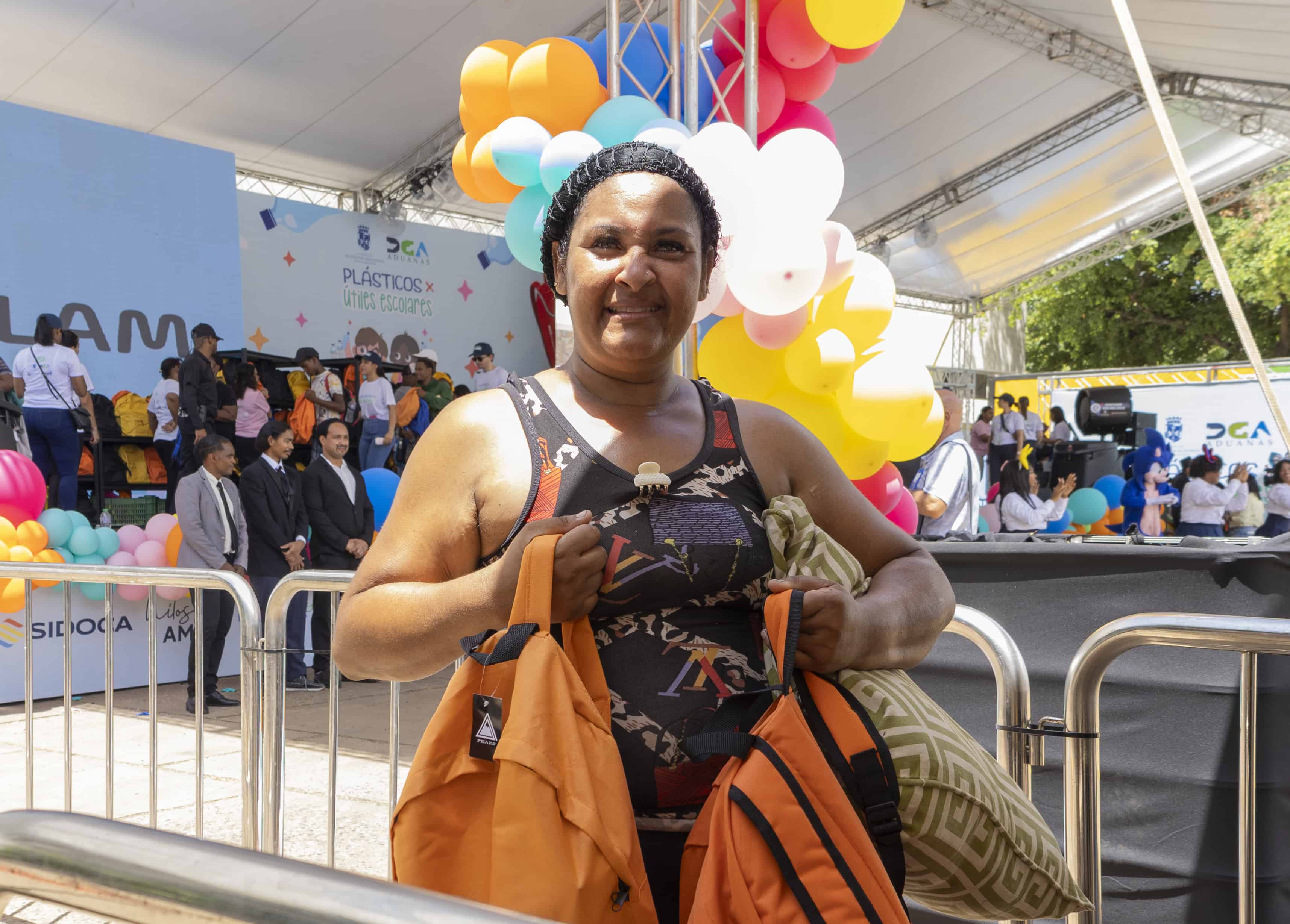 Una madre sostiene dos mochilas conseguidas luego de intercambiar los plásticos recolectados.