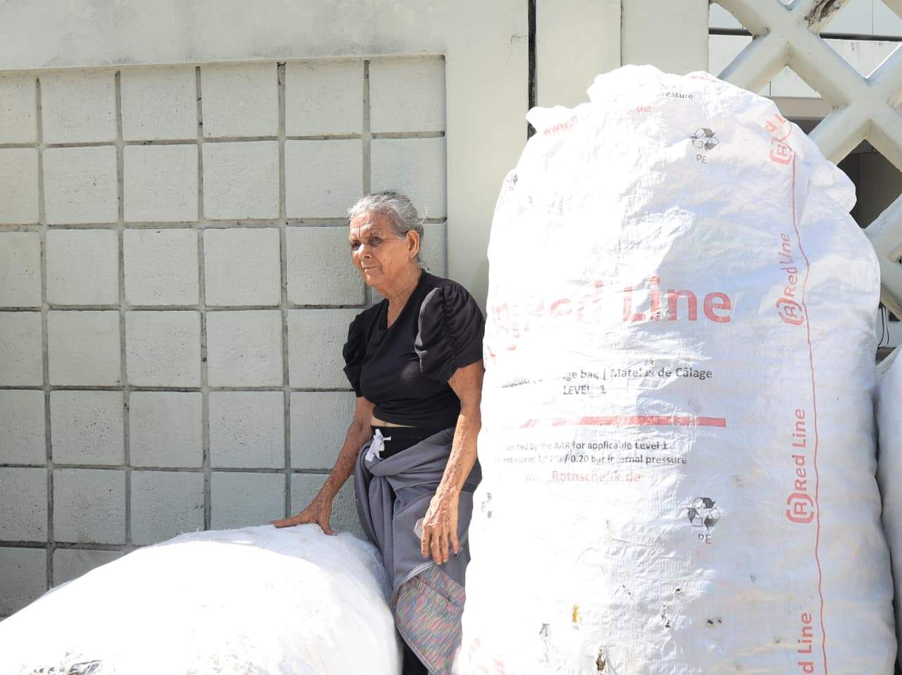 Una señora descansa entre grandes envases conteniendo los plásticos.