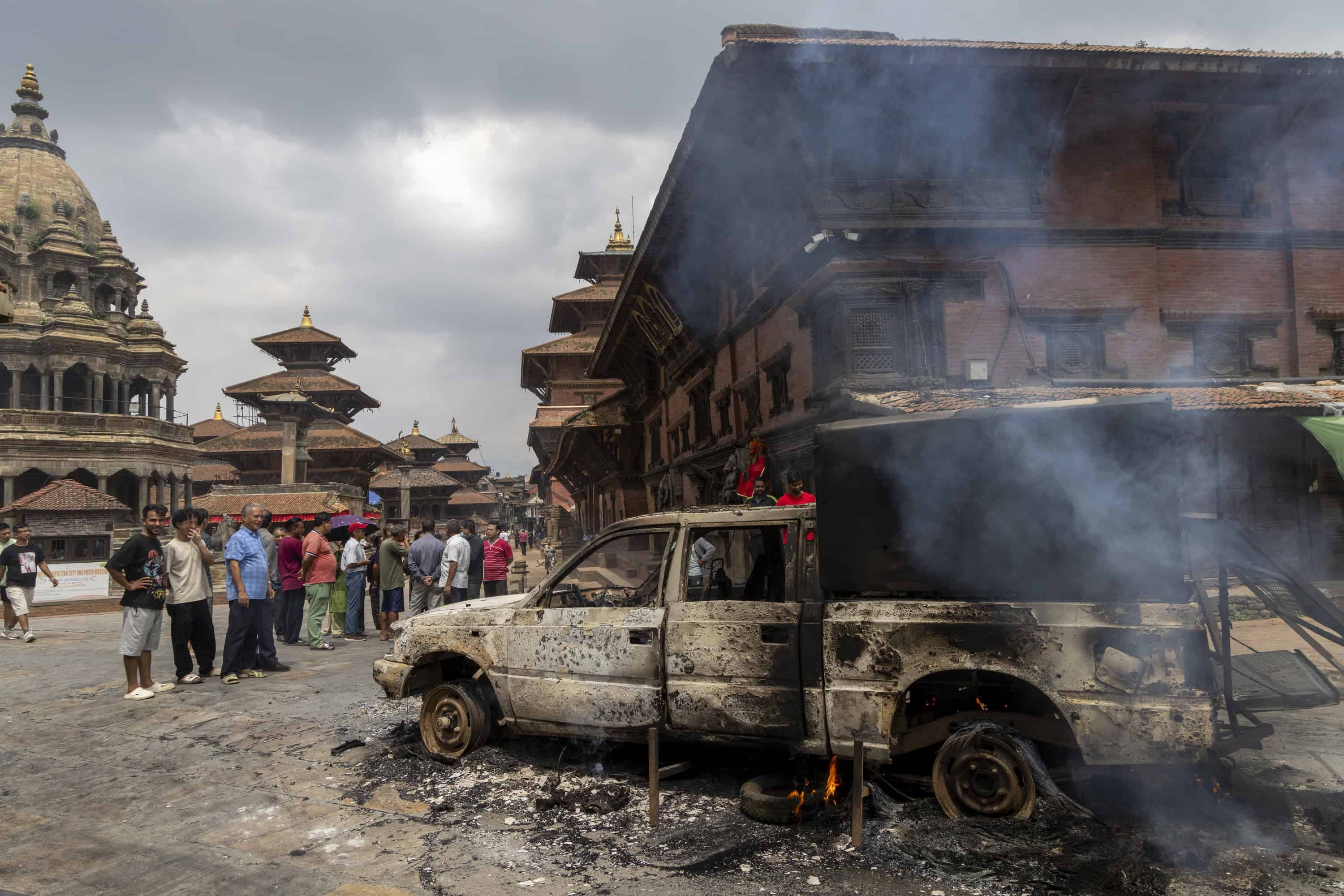 La gente se para junto a un vehículo gubernamental quemado tras los violentos enfrentamientos en Katmandú, Nepal, el 09 de septiembre de 2025. Al menos 19 personas murieron y docenas resultaron heridas el 8 de septiembre durante manifestaciones contra la corrupción y una prohibición de las redes sociales del gobierno. (Protestas)