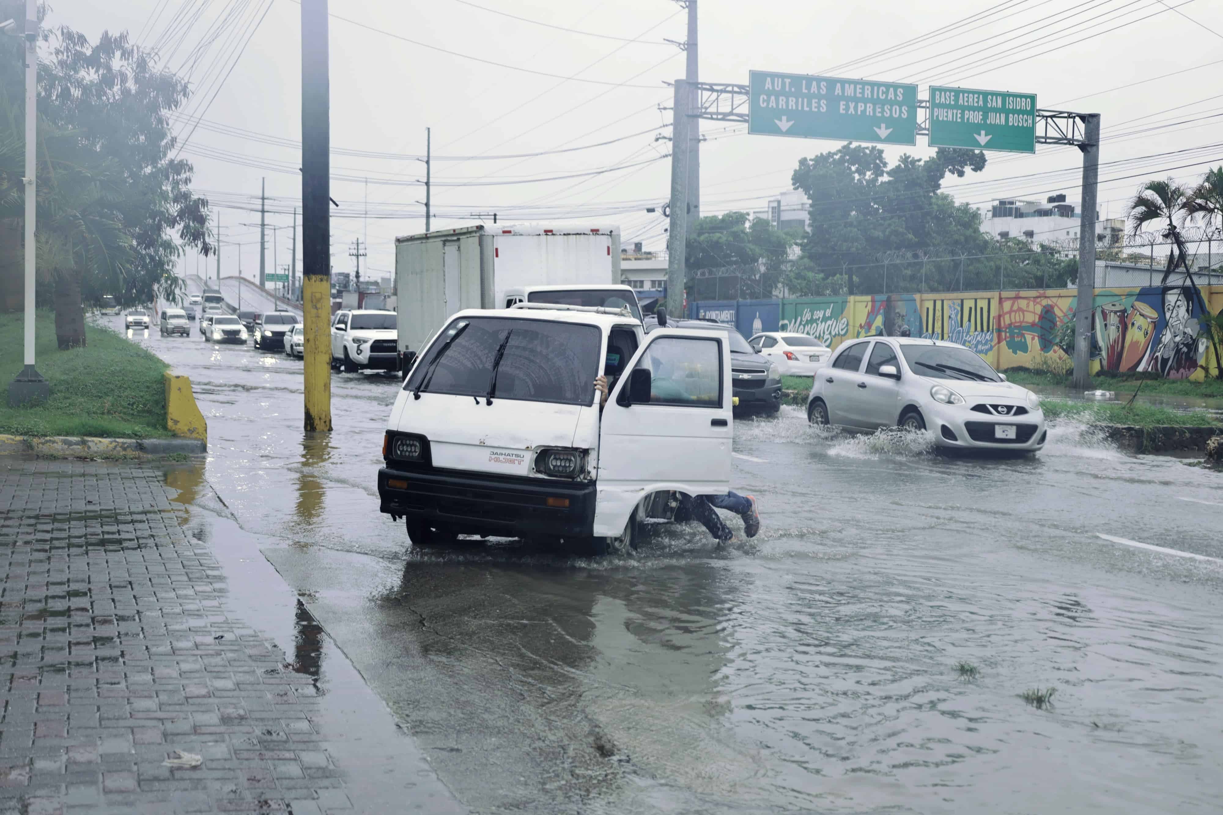 Un hombre empuja un pequeño vehículo de carga varado por la lluvia en la avenida Charles de Gaulle.