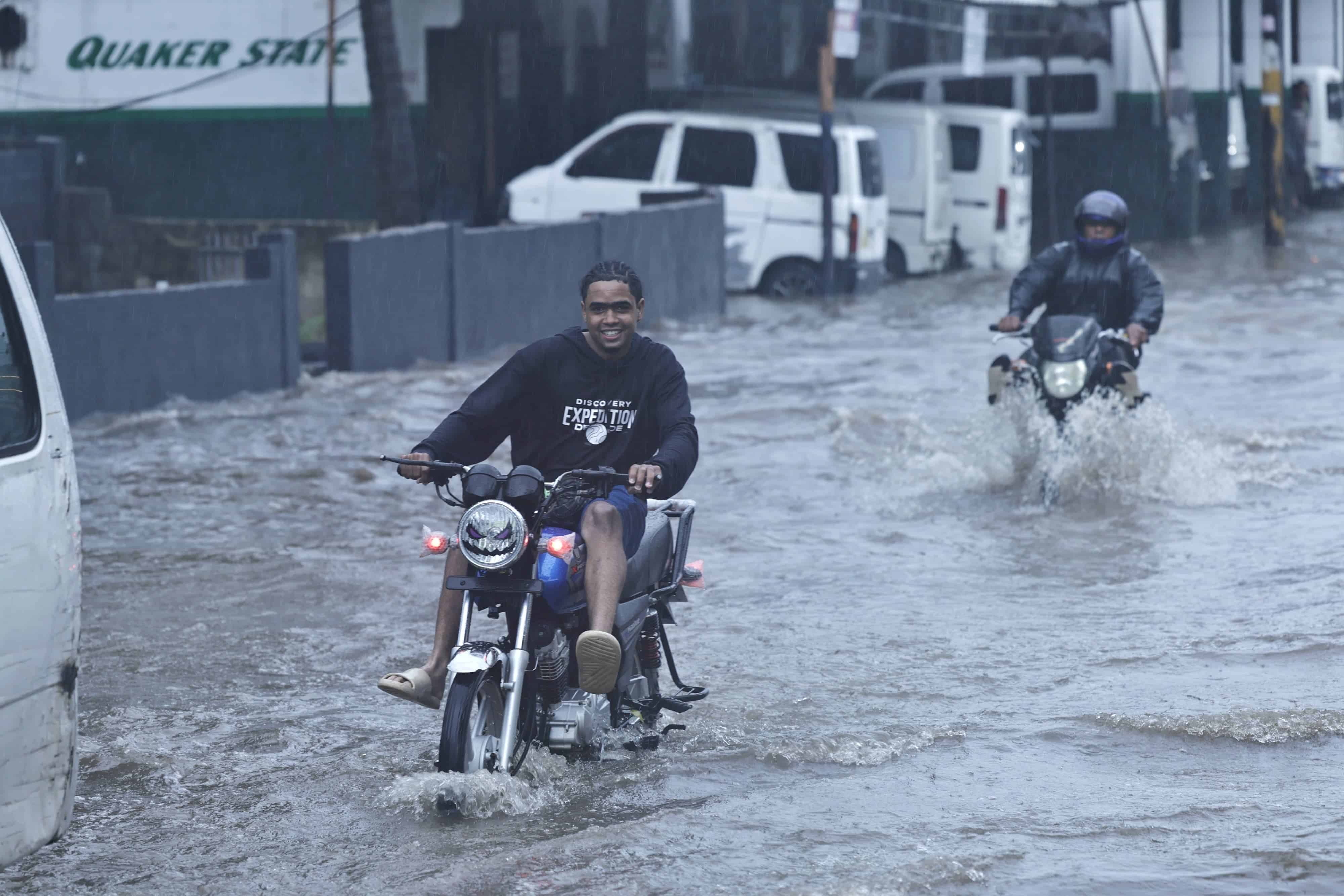Un motorista cruza un gran charco en la avenida Charles de Gaulle sin perder su sonrisa.