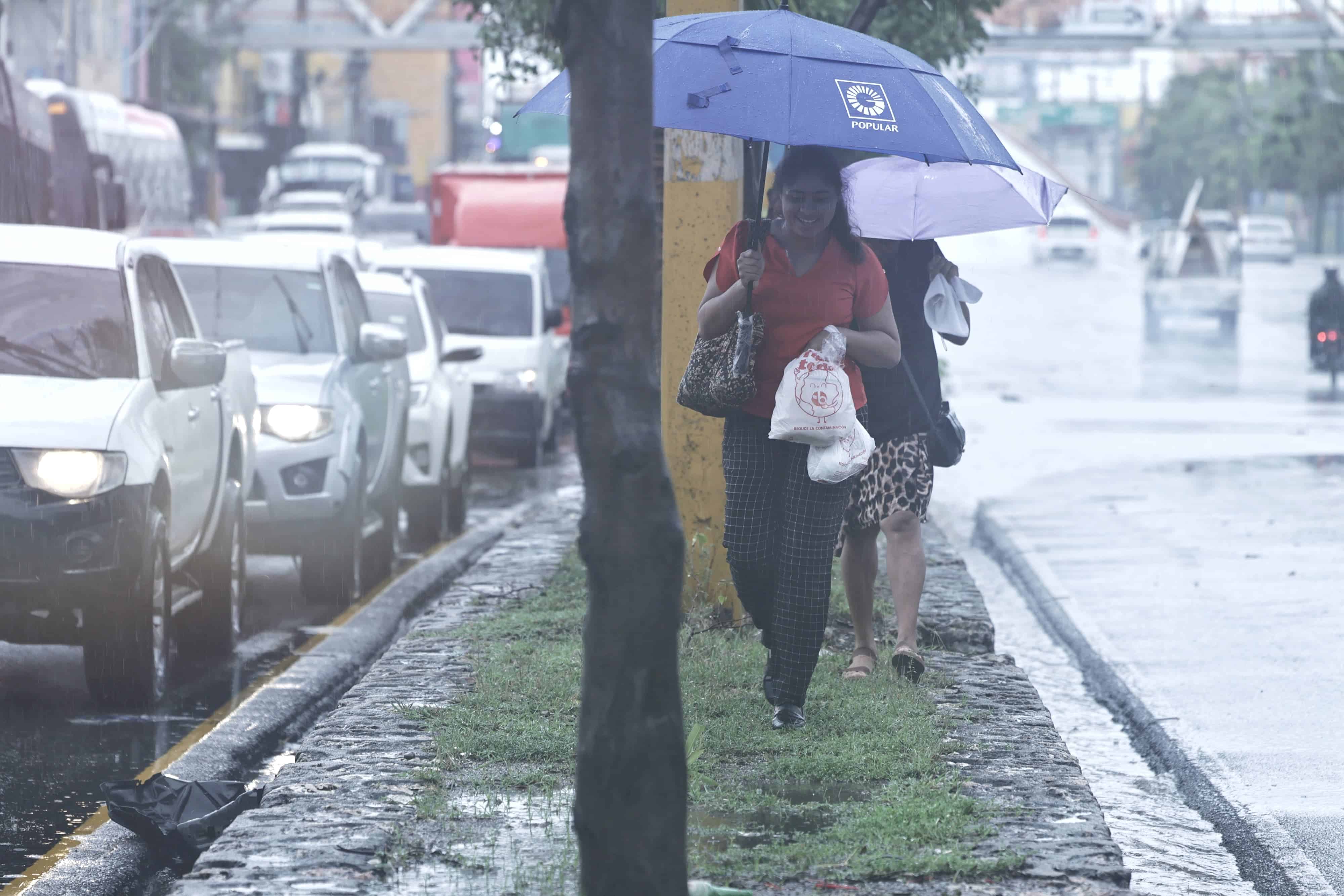 Dos mujeres cruzan la isleta de la avenida Charles de Gaulle mientras el agua y el tránsito se acumulan producto de las lluvias intensas que afectan el Gran Santo Domingo.