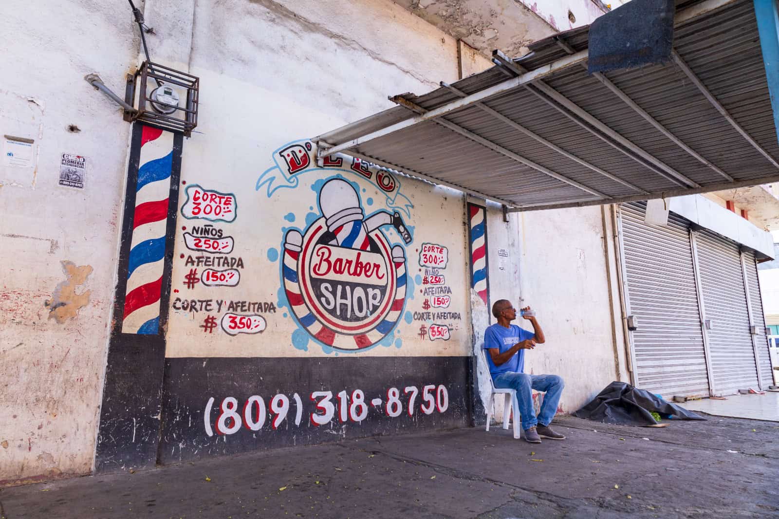 Una barbería en la acera, acomodada con techo de zinc, barandas y grafitis.