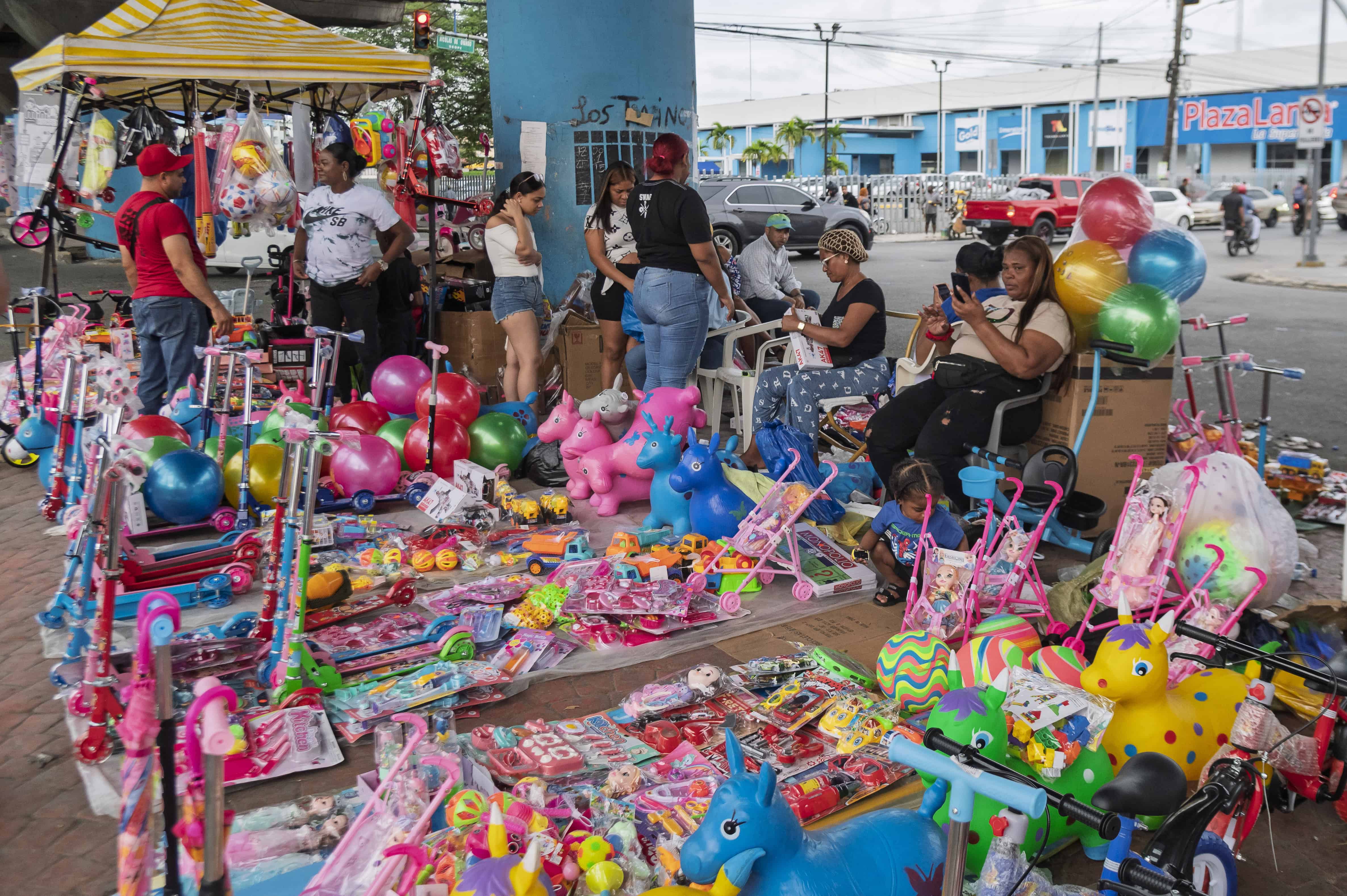 Un animado mercado callejero lleno de color, donde familias y vendedores se reúnen entre juguetes y sonrisas en la víspera del Día de Reyes.