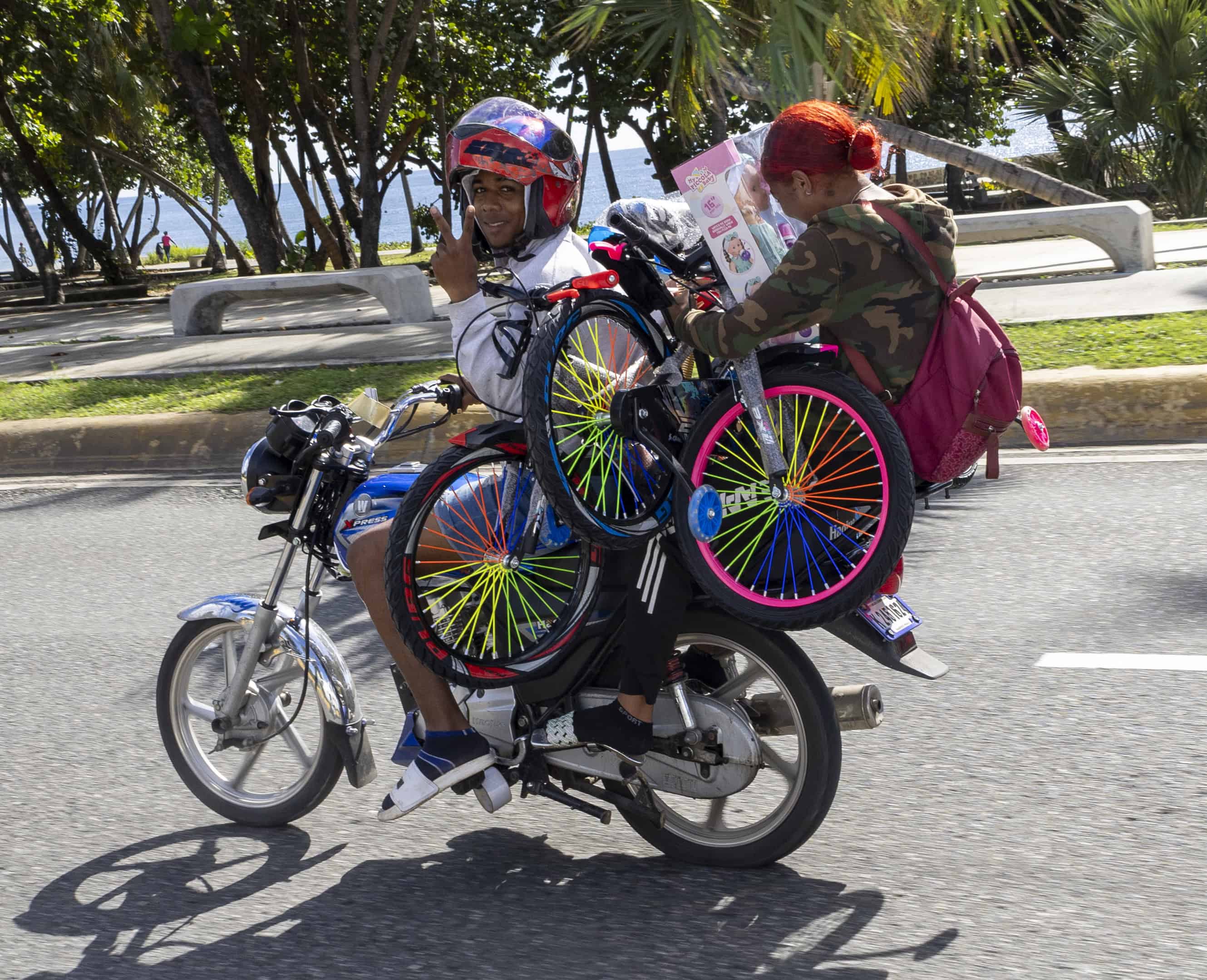Madre se transporta por la avenida George Washington en motocicleta, llevando dos bicicletas y un mu&ntilde;eco para sus hijos tras participar en el intercambio "Pl&aacute;sticos por Juguetes".<br>