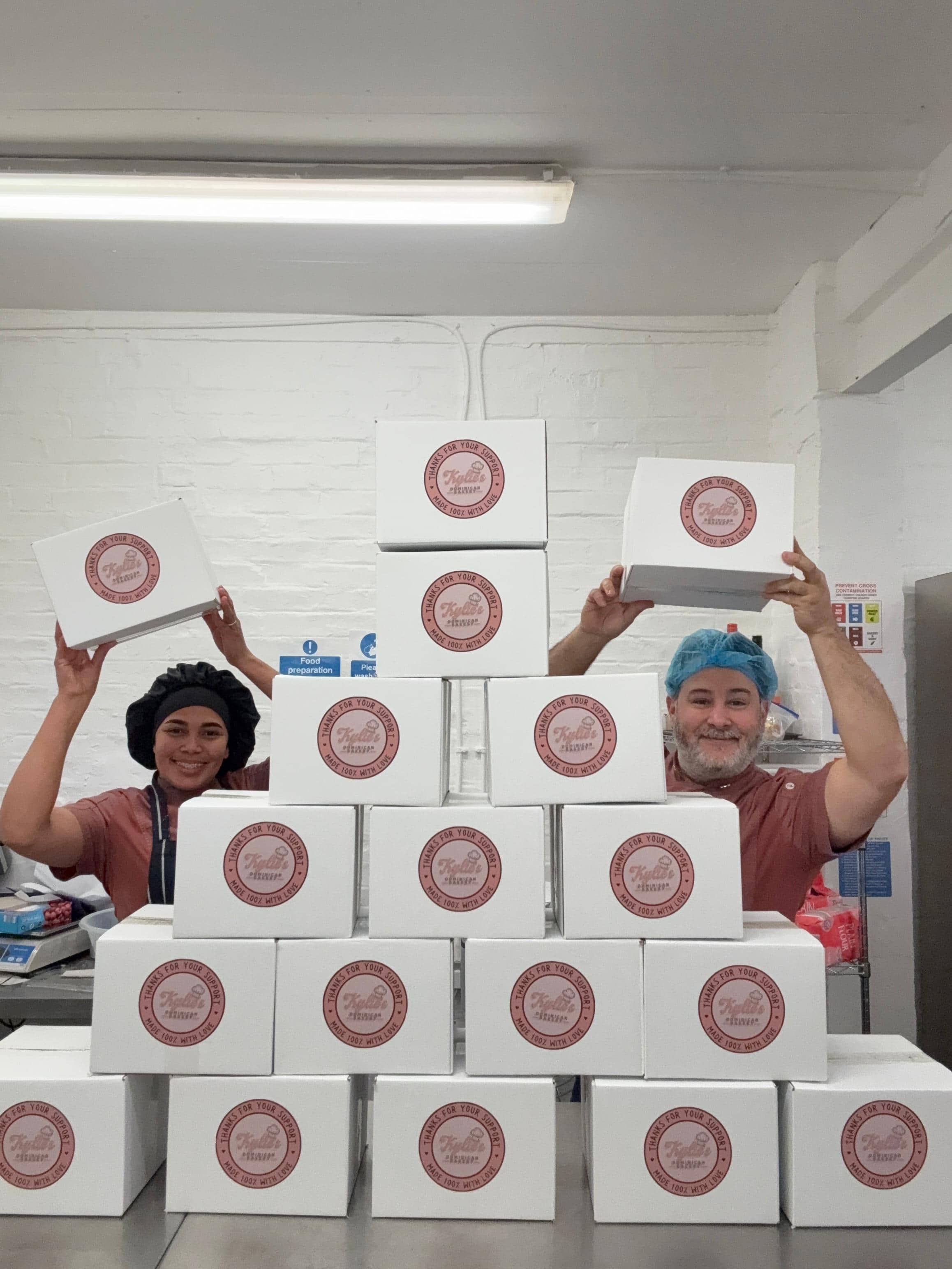 Luisa Sosa y Jos&eacute; Casanovas entre cajas rotuladas con el logo de Kylie's Dominican Bakery.