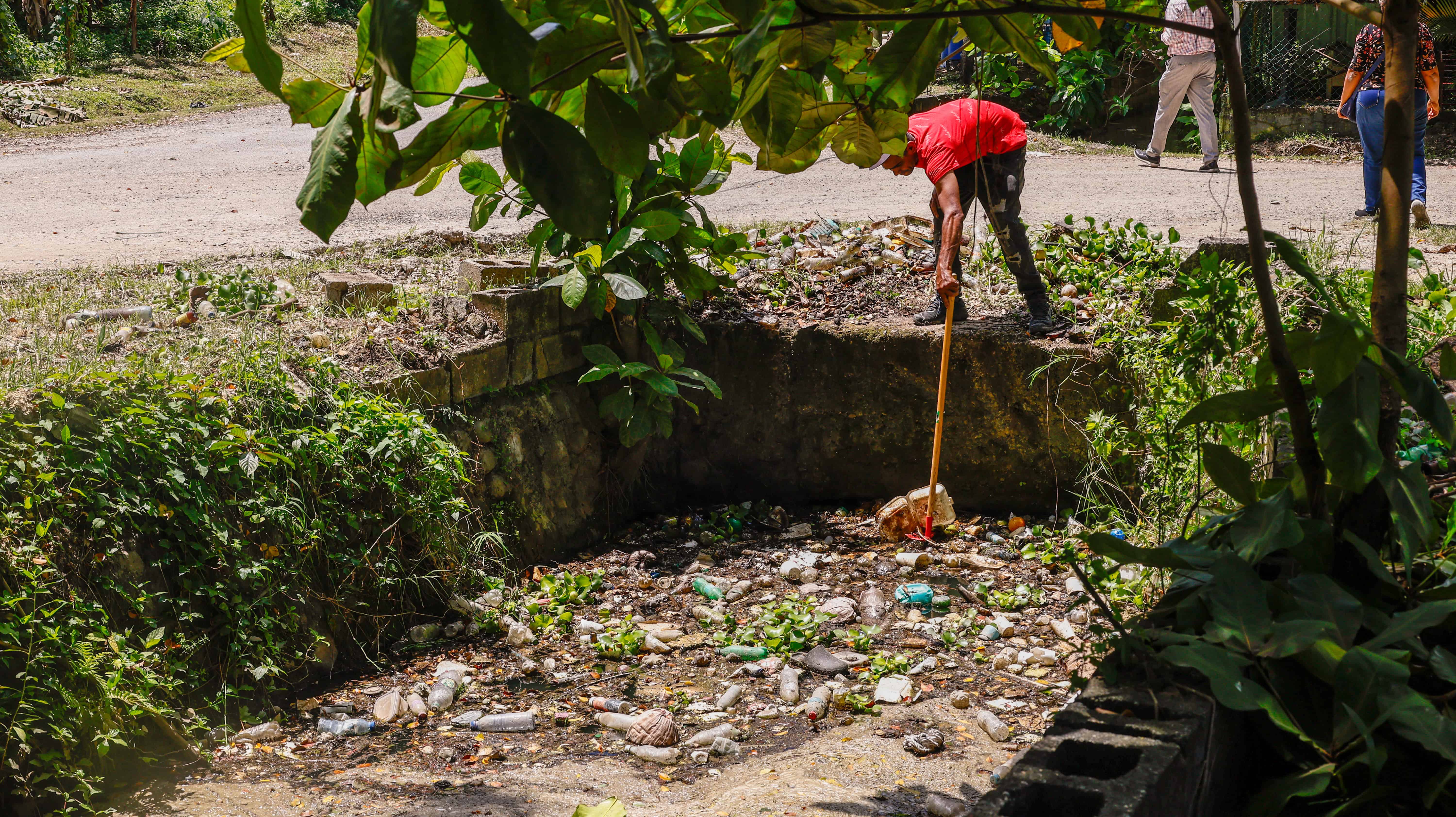 Los vecinos retiran postes pl&aacute;sticos y otros residuos del canal por donde corre el agua.
