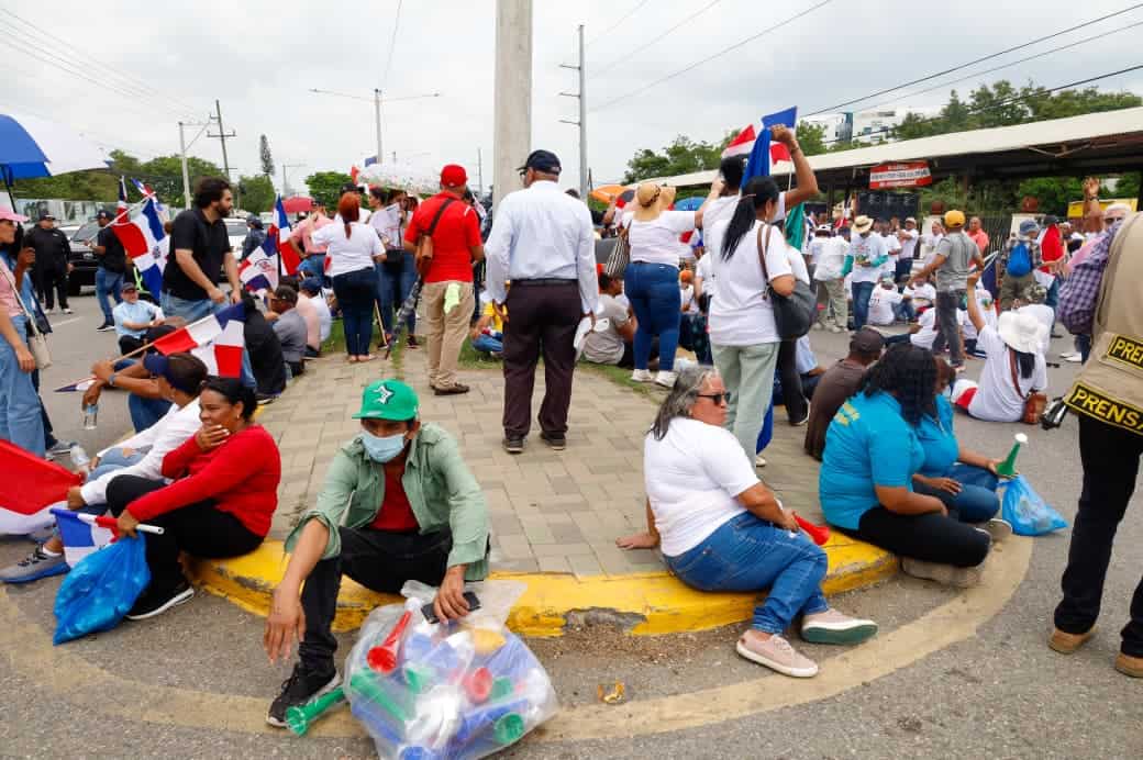Manifestantes se sientan en la acera y la calle durante el bloqueo de la autopista Duarte, exigiendo que se suspenda la actividad minera en la Cordillera Septentrional.