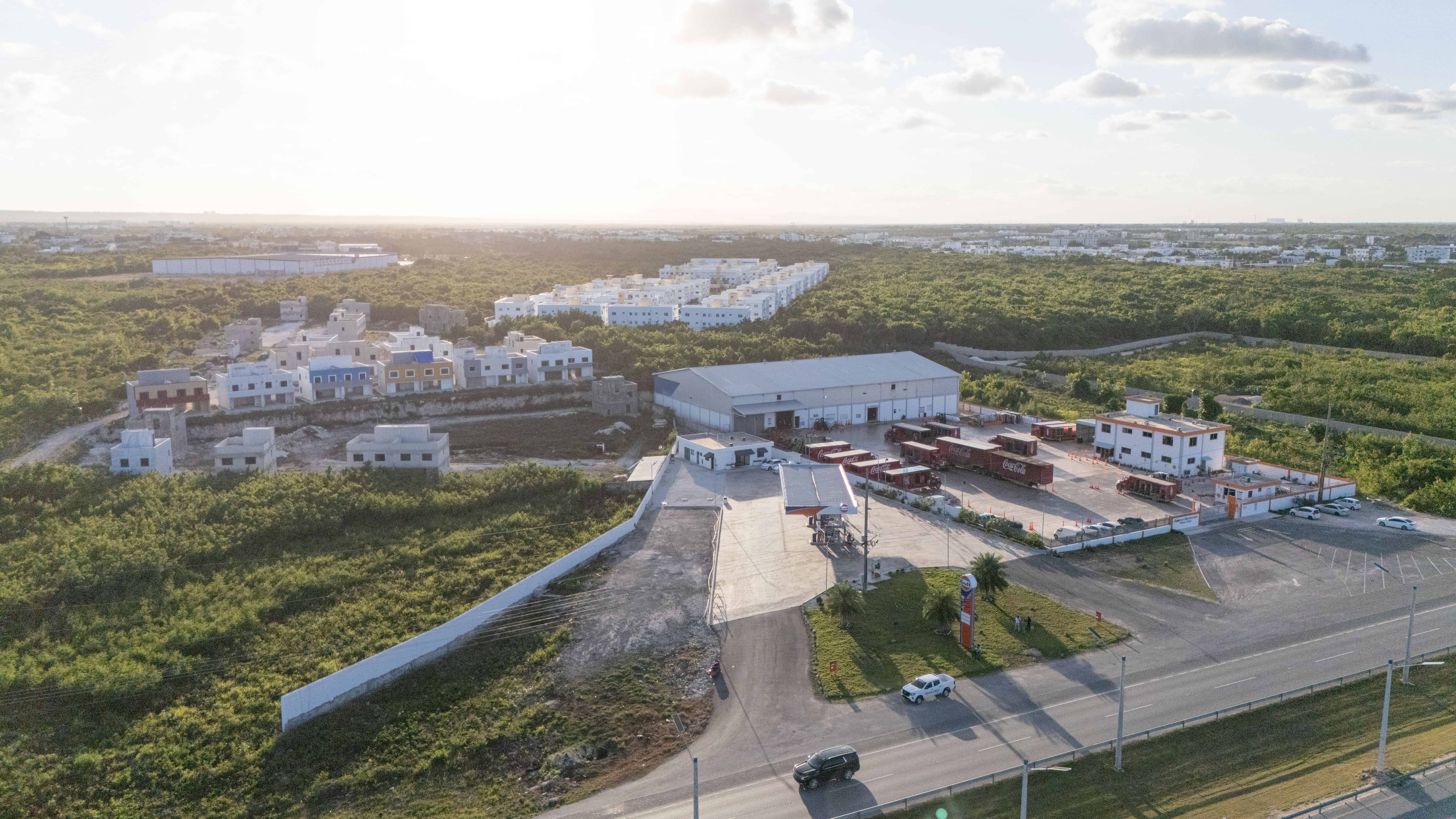 Vista aérea de dos condominios, en los que se observa el de más reciente construcción justo detrás de una estación de gasolina y al lado de una embotelladora.