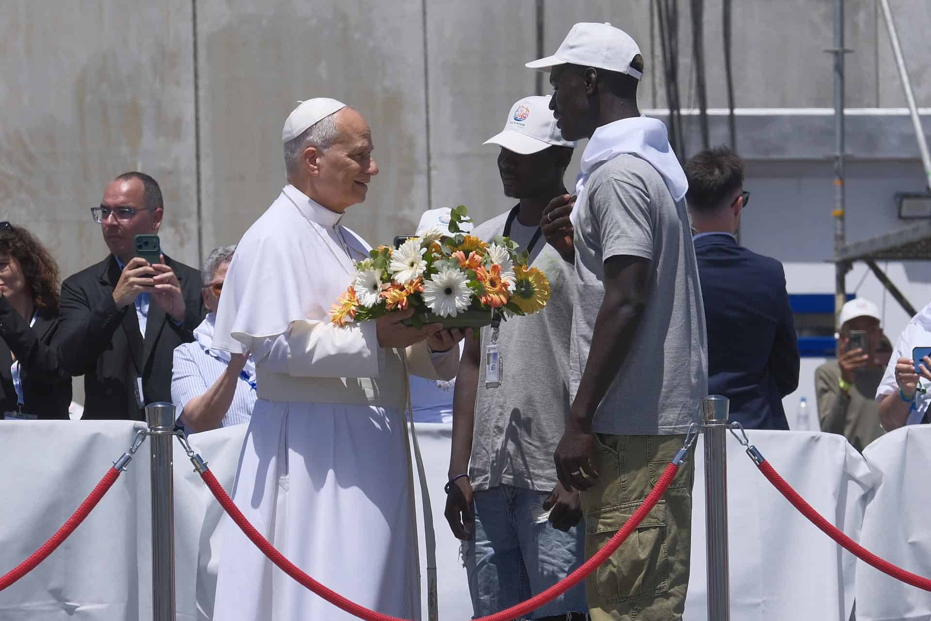 El papa Le&oacute;n XIV recibe flores de dos voluntarios para protagonizar una ofrenda floral en el mar en recuerdo de los migrantes muertos en la traves&iacute;a durante el encuentro con m&aacute;s de un millar de inmigrantes de &Aacute;frica, Am&eacute;rica Latina y con representantes de las principales instituciones y organizaciones sociales que trabajan en los servicios de rescate, acogida e integraci&oacute;n en el muelle de Arguinegu&iacute;n, en la isla de Gran Canaria, este jueves, en el sexto d&iacute;a de su viaje a Espa&ntilde;a.