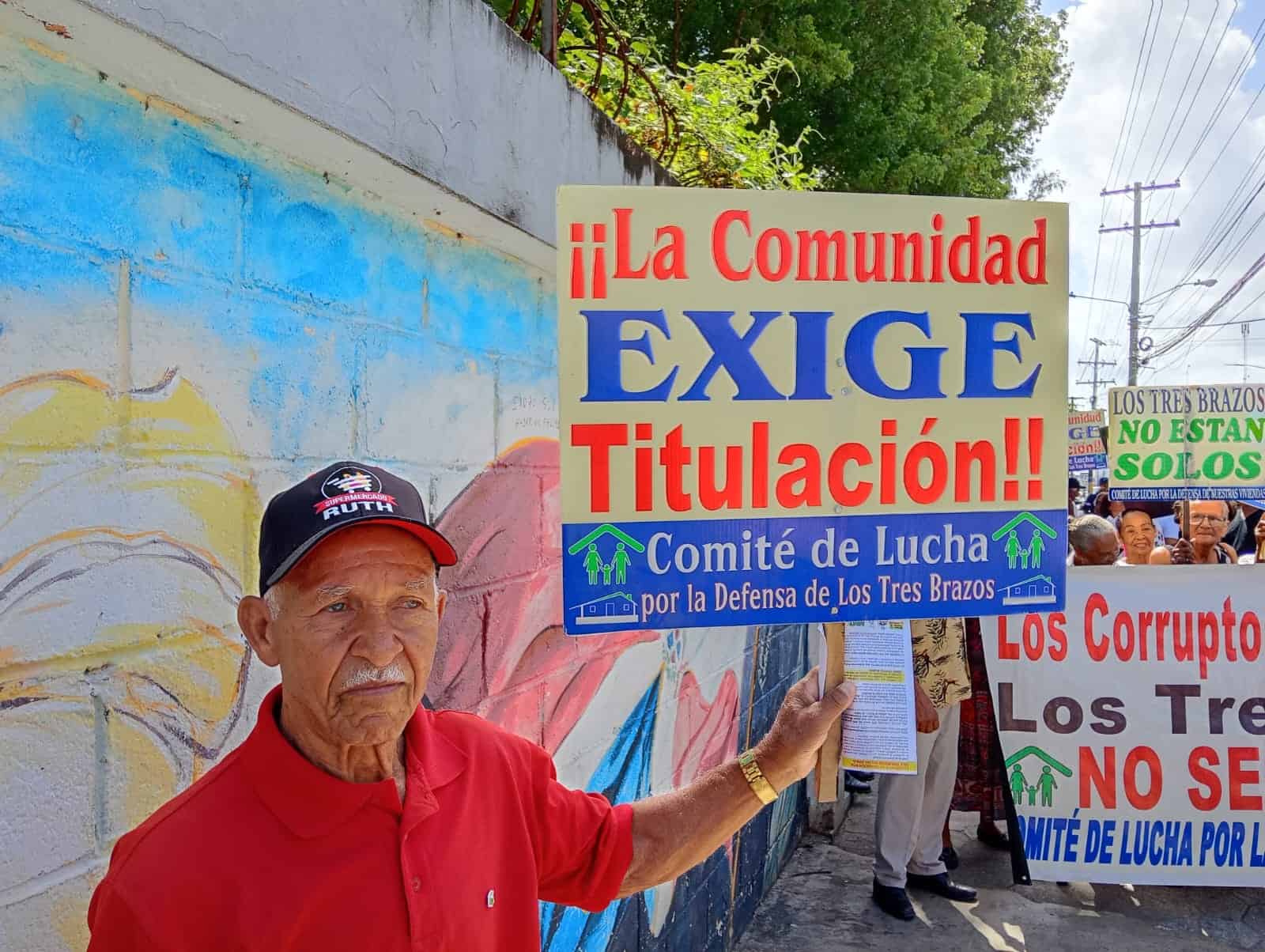 Un hombre muestra un cartel en el que exige que se les otorgue la titulaci&oacute;n de los terrenos que ocupan en el sector Los Tres Brazos.