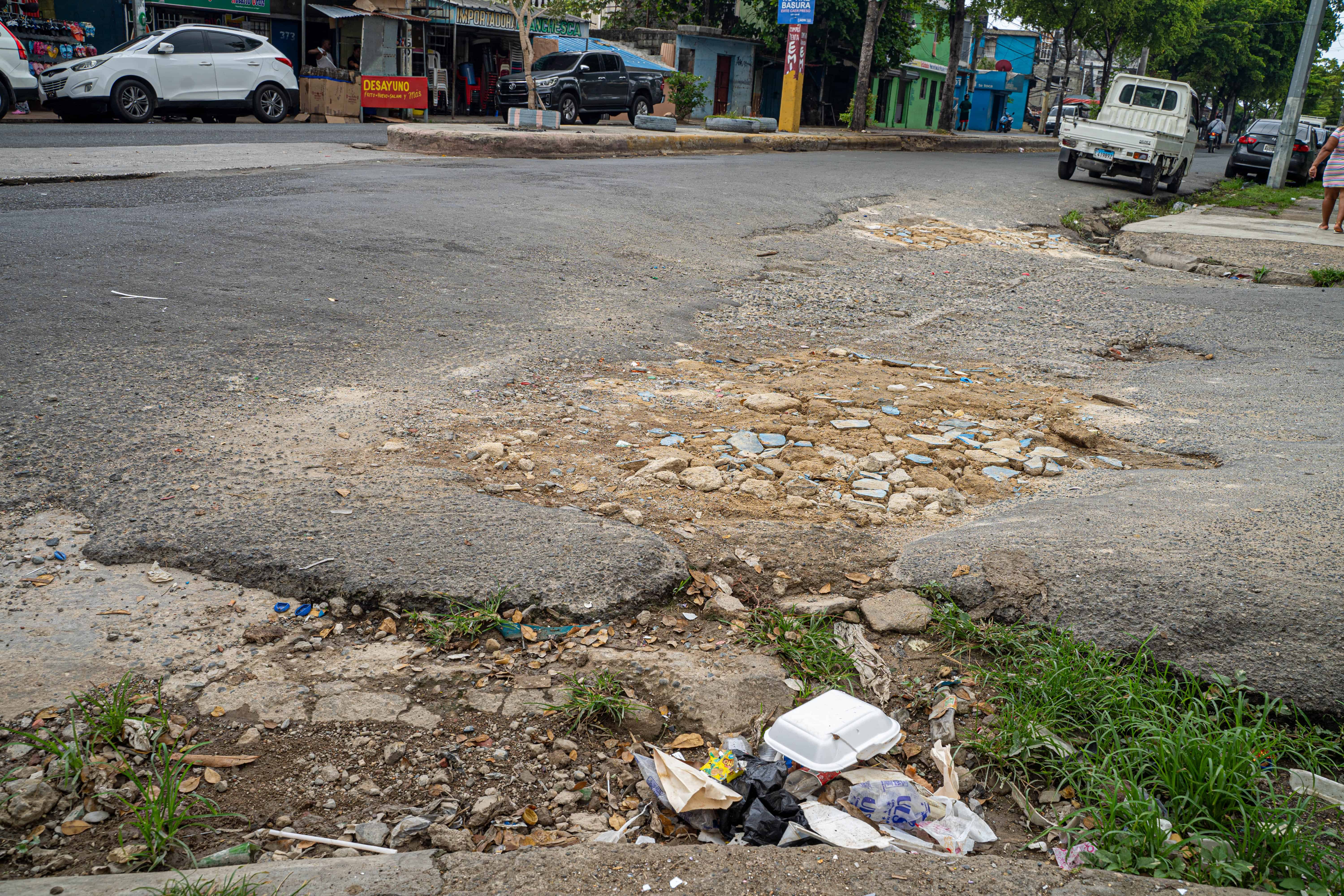 Piedras y cartones deteriorados colocados por residentes advierten sobre los baches en la calle Santa Cruz, en Guachupita.