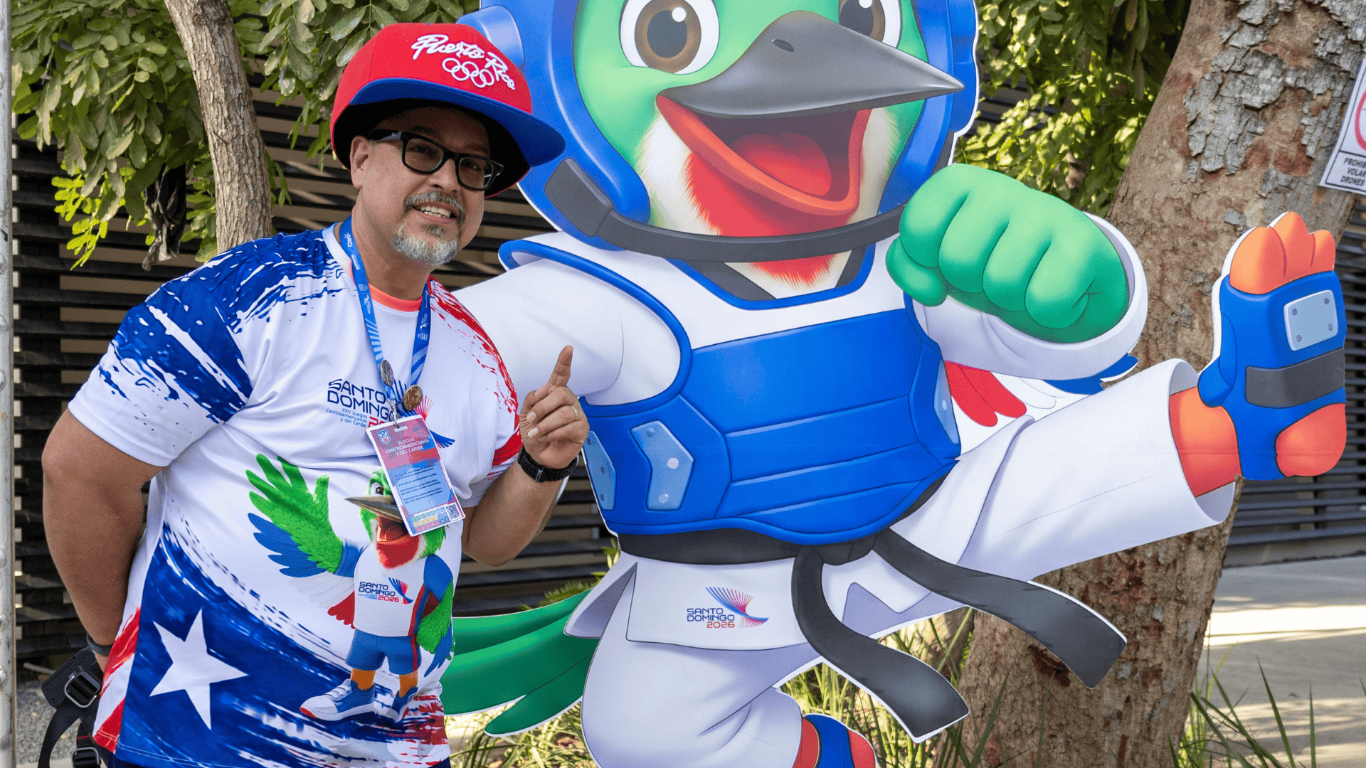 Rafael posa con Col&iacute;, mascota de Santo Domingo 2026, en la entrada del pabell&oacute;n de taekwondo del Centro Ol&iacute;mpico Juan Pablo Duarte.