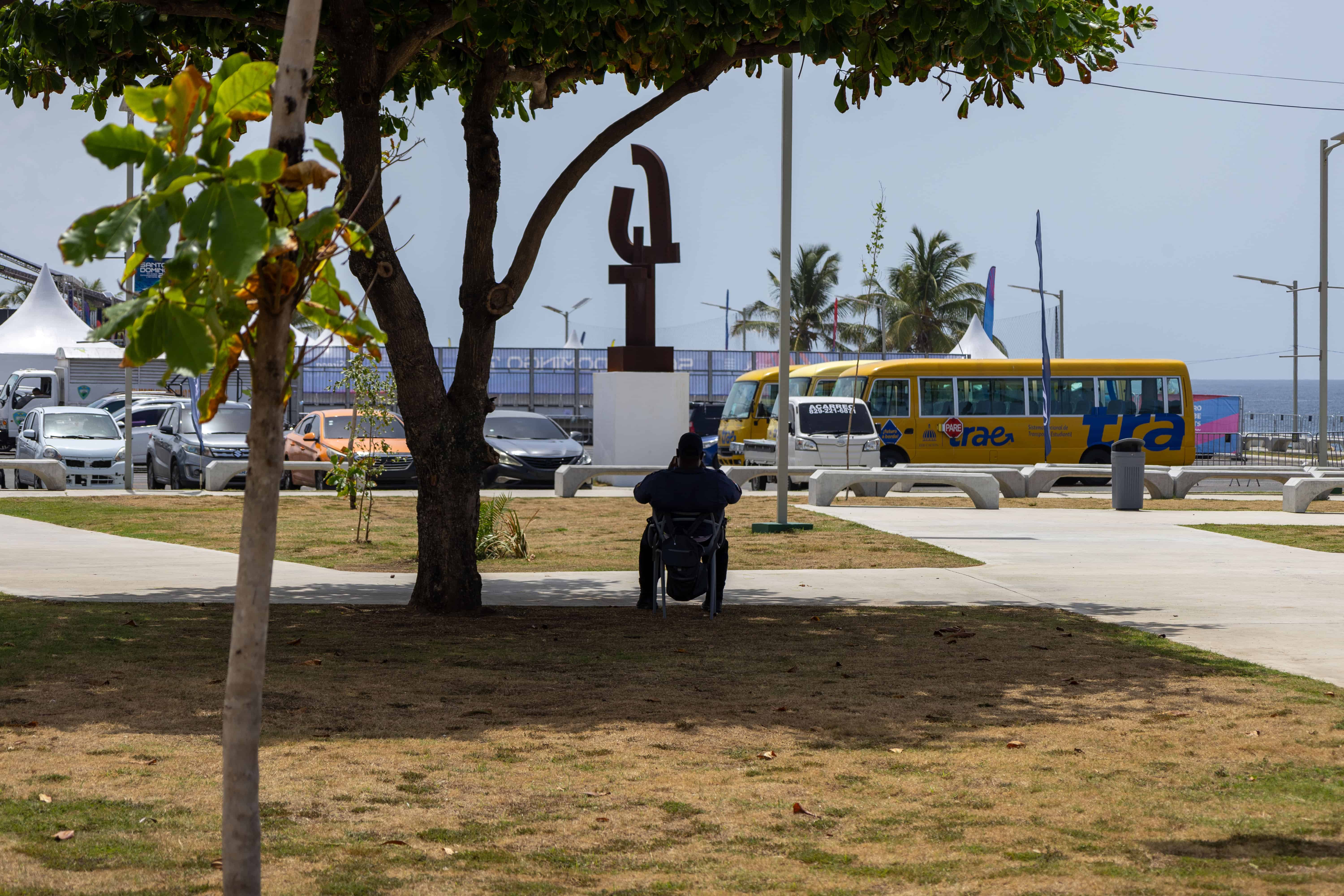 Agente de seguridad sentado bajo la sombra de uno de los pocos árboles dentro del Malecón Deportivo.