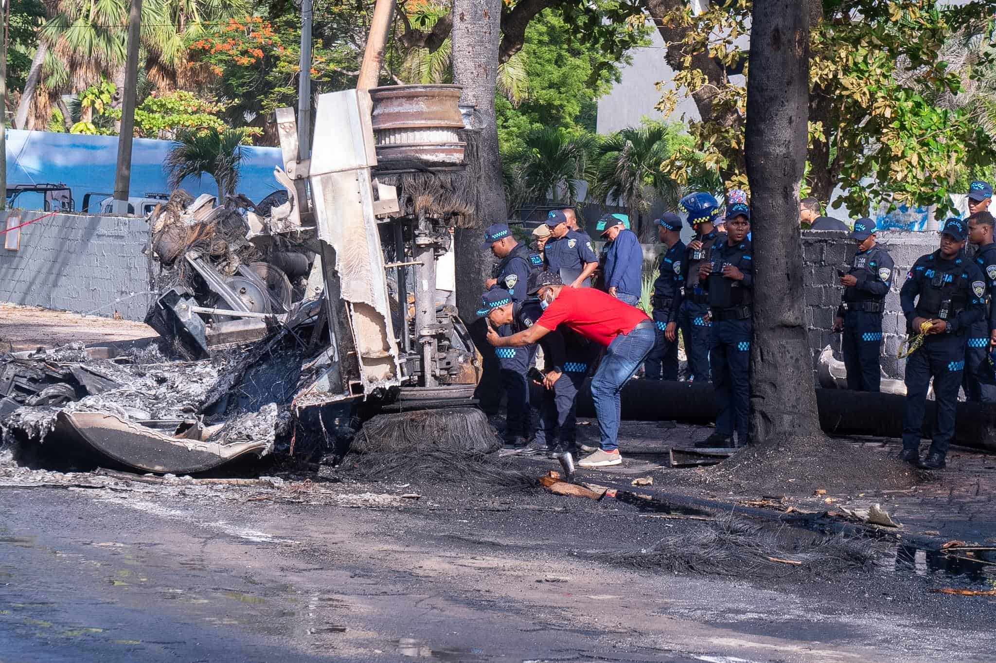 Personas observan los vehículos calcinados y la escena del accidente ocurrido este lunes en la avenida George Washington, donde dos personas perdieron la vida.