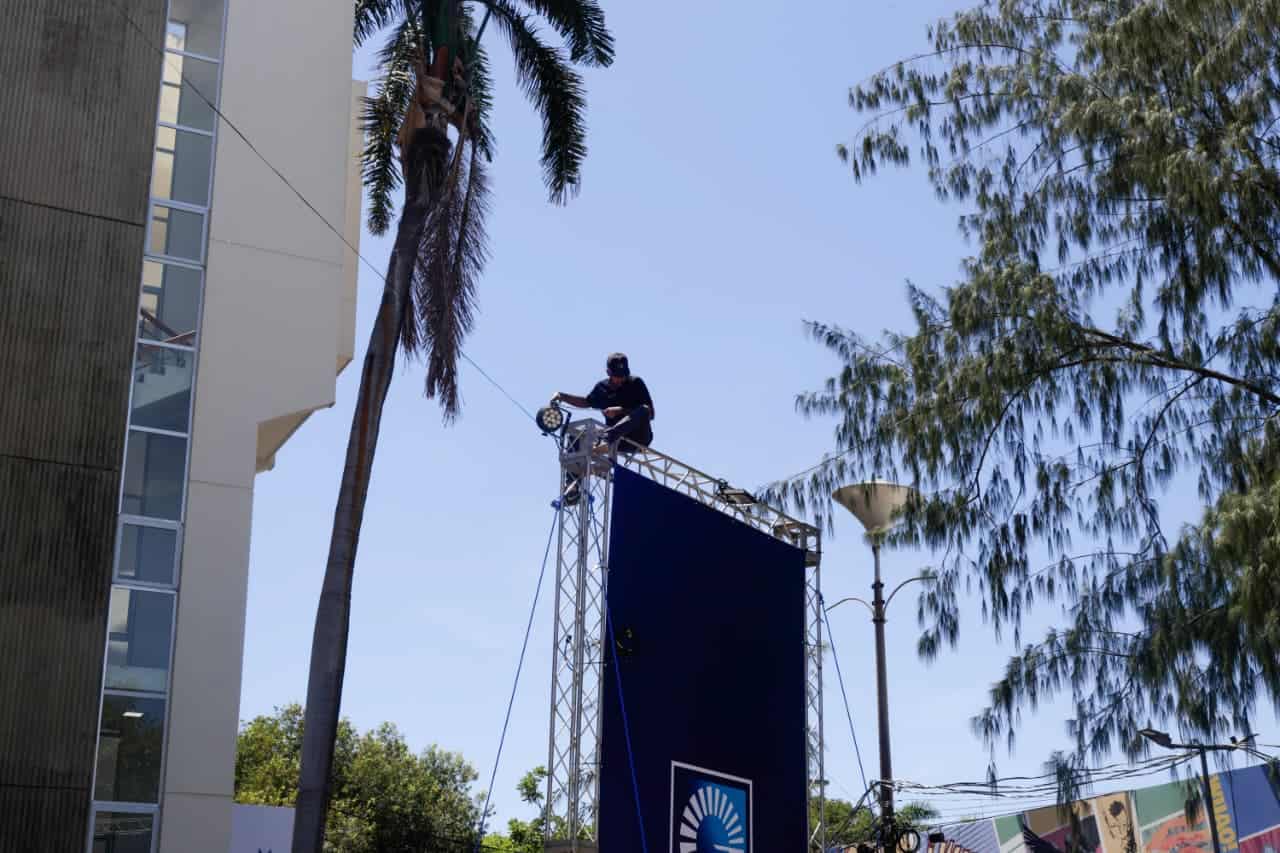 Un joven trabaja en el montaje de luces sobre una valla publicitaria en el recinto de la feria.