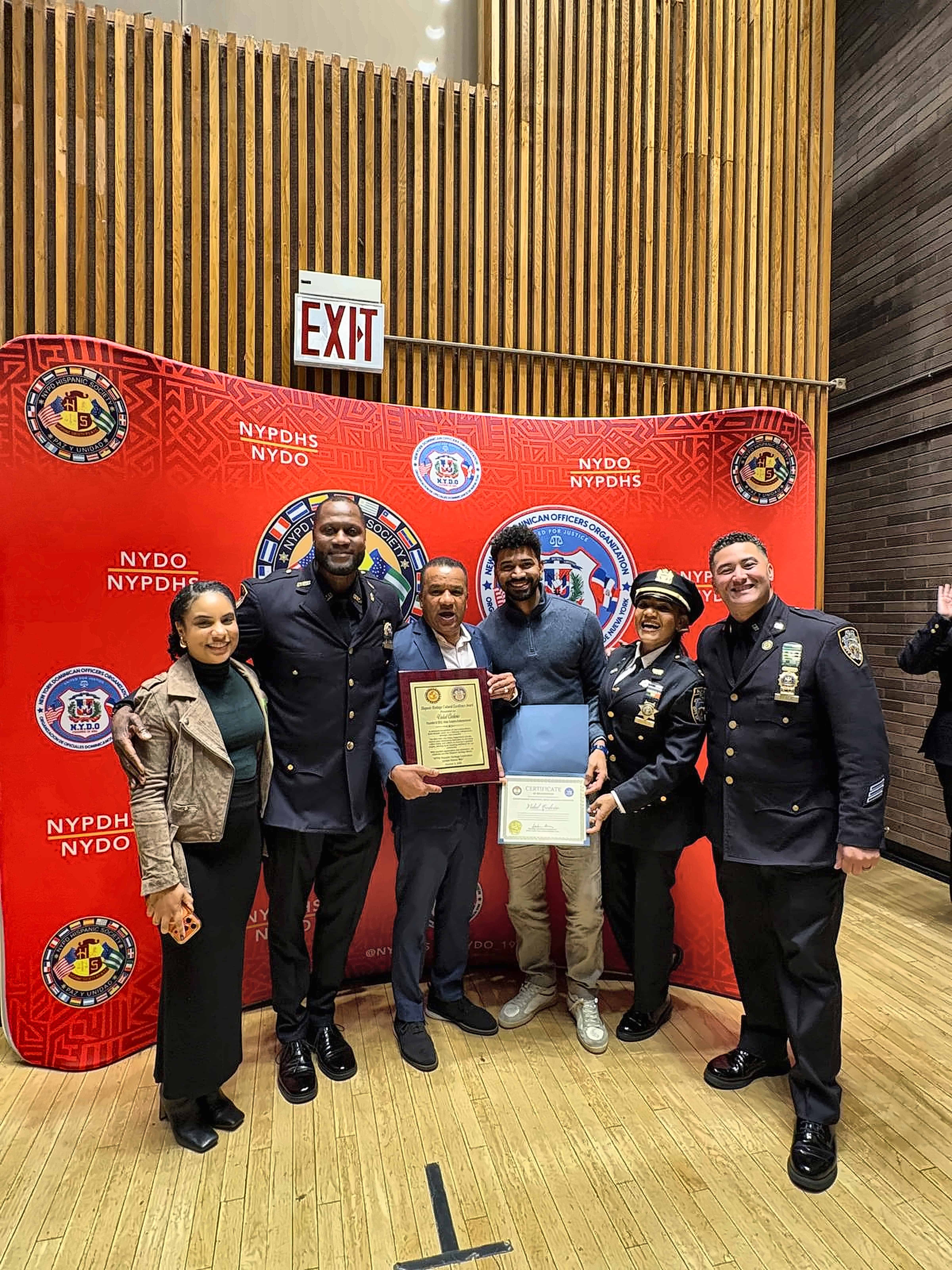 Vidal Cedeño muestra el reconocimiento recibido de la sociedad hispana del Departamento de Policía de Nueva York (NYPD), acompañado por oficiales y familiares durante el acto celebrado en Nueva York.