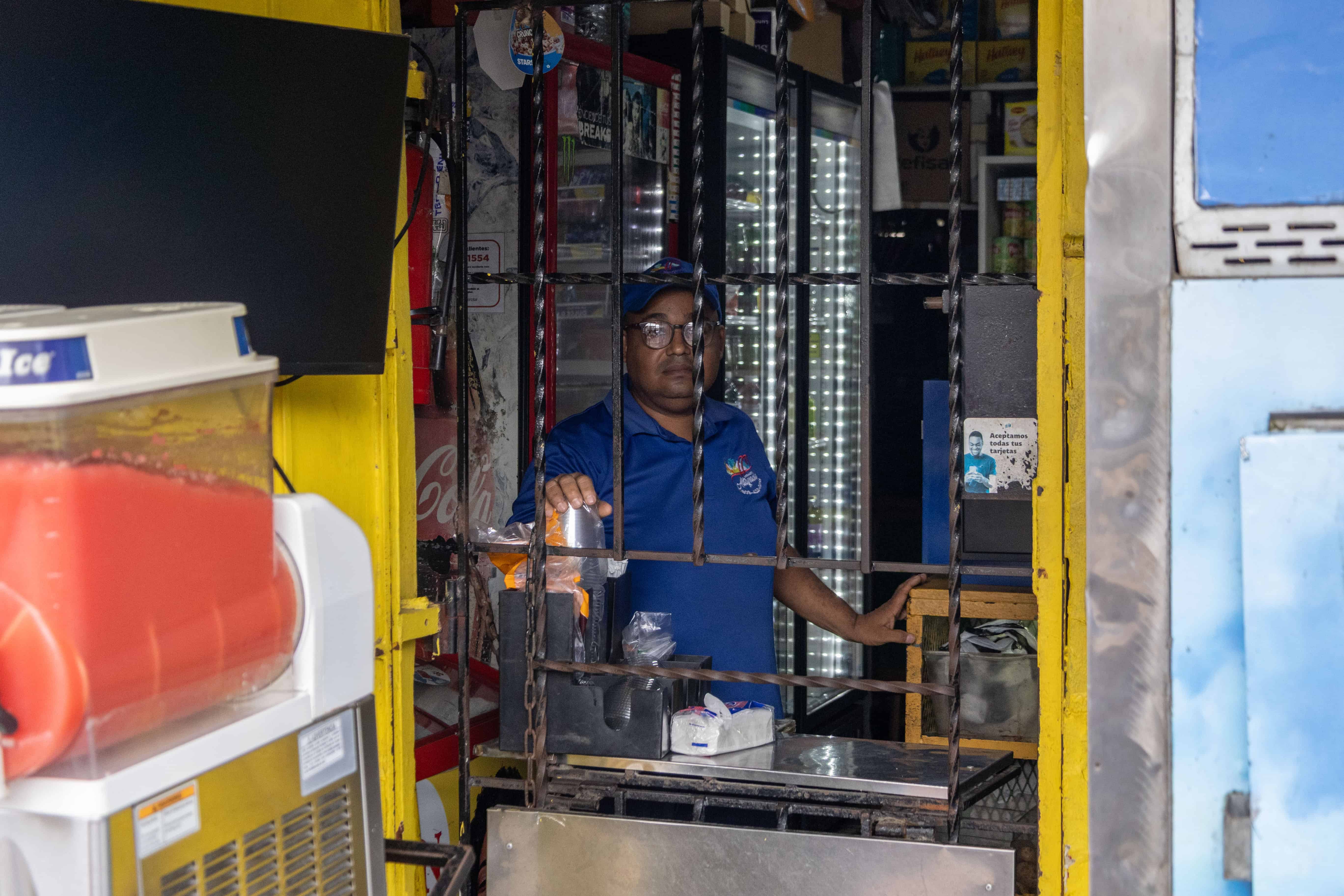 Yeison brinda sus servicios detr&aacute;s de la verja de su mostrador.