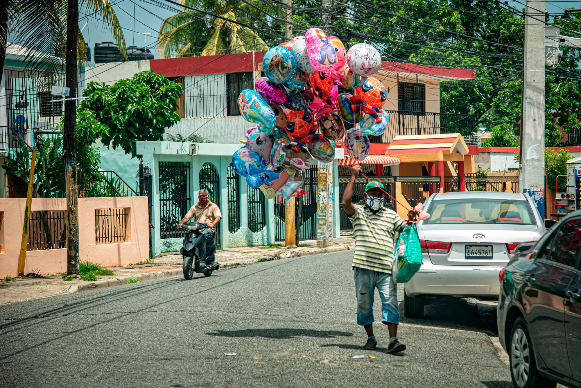 En la imagen un hombre carga globos para niños llenos de helio. El vendedor transita por las calles de los barrios buscando vender juguete como medio de subsistencia.