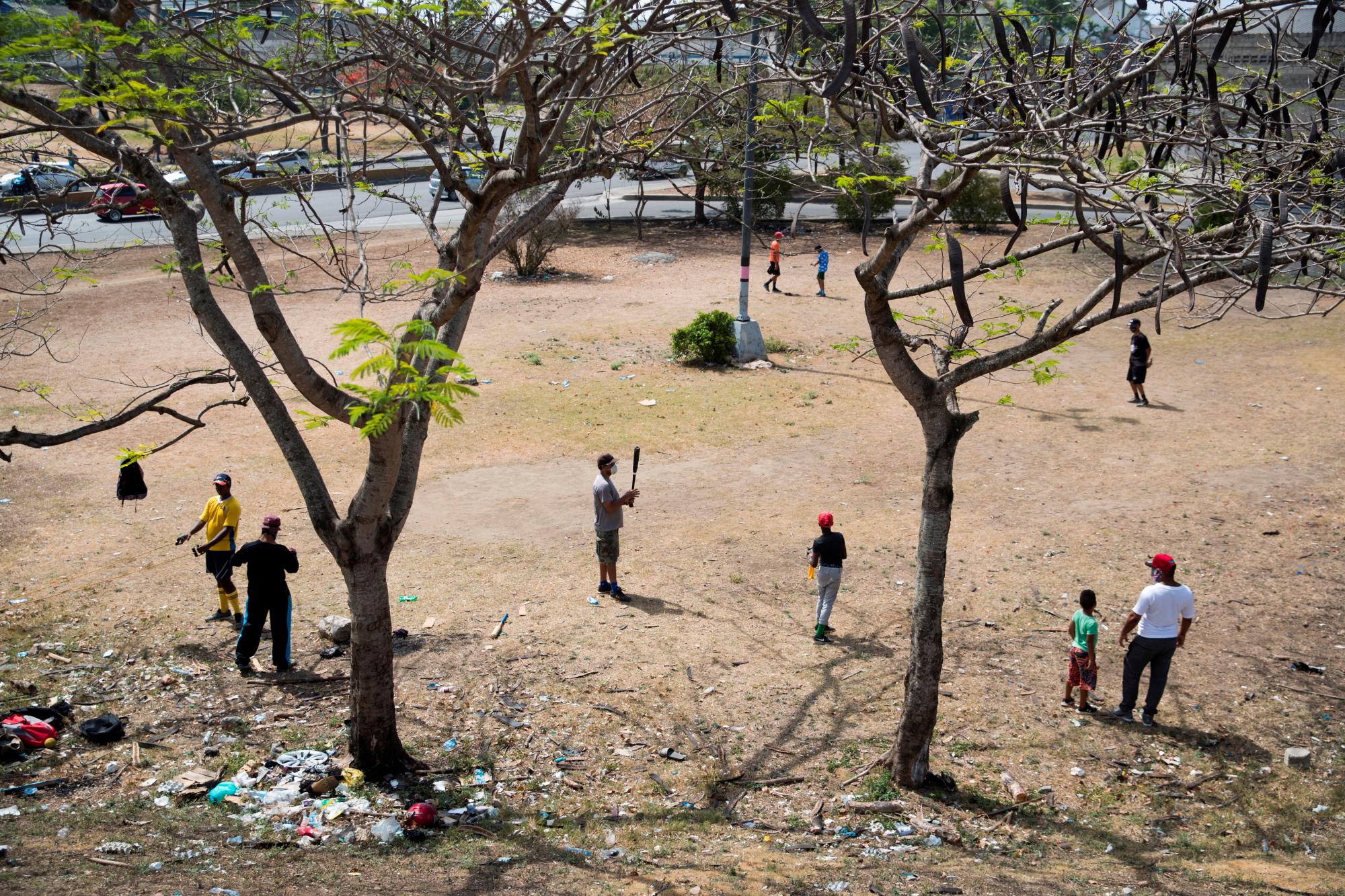 Jóvenes practican béisbol este viernes en un parque en Santo Domingo (República Dominicana). Un batazo tras otro, las pelotas siguen volando en Santo Domingo, una de las principales capitales del béisbol del Caribe. Pero ahora, en tiempos de coronavirus, no vuelan la cerca del play sino que aterrizan en las carreteras o, de vez en cuando, en los faros de un automóvil. Y es que la pandemia ha obligado al béisbol amateur a buscar refugio en las calles, en los descampados, lejos de las canchas, cerradas hace ya dos meses. EFE/Orlando Barría