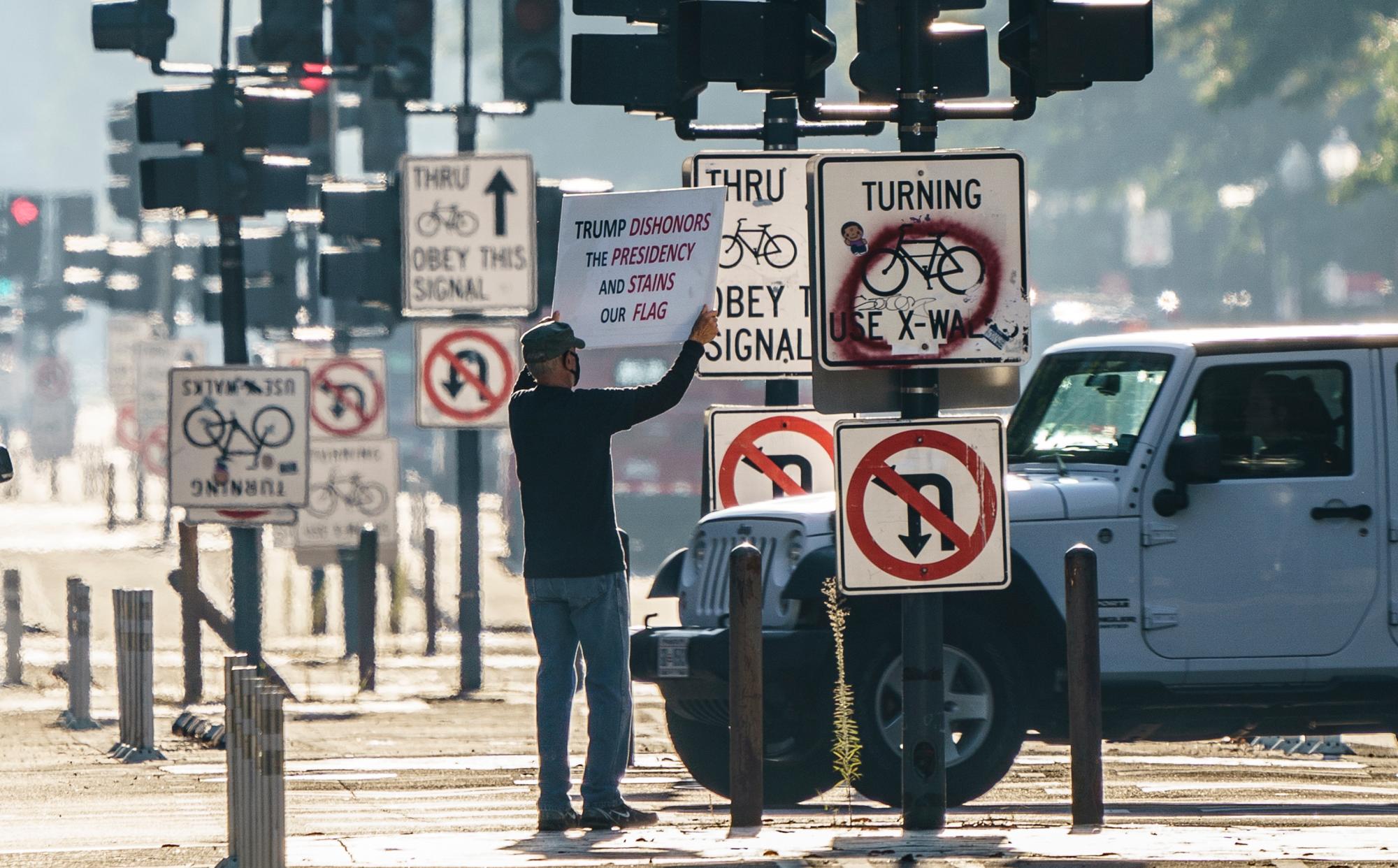 Peter Matlon, residente de Washington, sostiene un letrero de protesta para que los viajeros lo vean en la avenida Pennsylvania cerca del Trump Internacional Hotel en Washington, el miércoles 7 de octubre de 2020 por la mañana durante las elecciones, pero se vio obligado a cambiar de táctica debido a la pandemia de COVID-19.