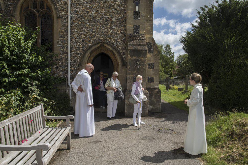 El reverendo Jonathan Gordon, izquierda, y la vicaria adjunta Miranda Shelton reciben a feligreses anglicanos en su primer oficio comunitario al mitigarse la cuarentena de la pandemia en la igleia de Santa María en Northchurch in Berkhamsted, Inglaterra, 5 de julio de 2020. La pandemia nos obligó a repensar todo, dice Gordon. (AP Foto/Elizabeth Dalziel)
