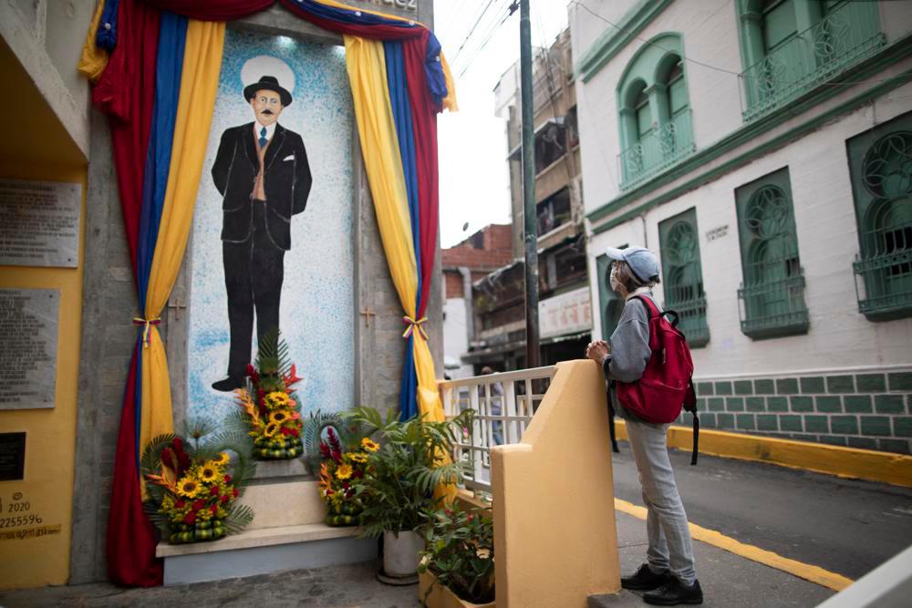 Una mujer reza cerca de un cuadro con la imagen de José Gregorio Hernández en la calle en la que falleció en un accidente de auto en 1919, en el vecindario de La Pastora, en Caracas, Venezuela, el 28 de abril de 2021. Conocido como el 'médico de los pobres', Hernández será beatificado el 30 de abril por la Iglesia católica, un paso hacia su santidad. 