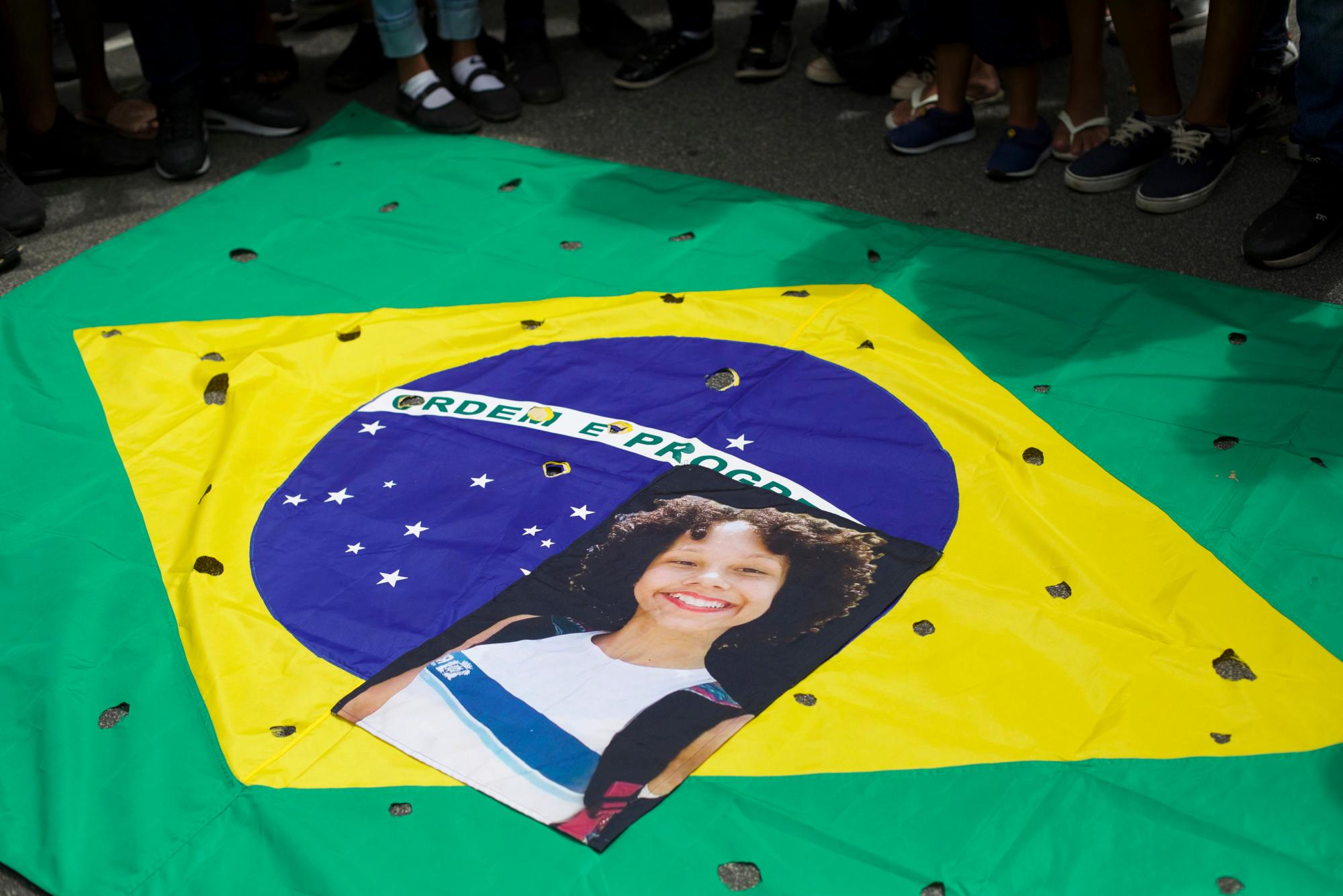 En imagen del miércoles 20 de marzo de 2019, una fotografía de la estudiante asesinada Maria Eduarda, que murió baleada durante un tiroteo en la escuela, es colocada sobre una bandera brasileña con orificios que simbolizan orificios de bala, durante una protesta organizada por la ONG Río de Paz afuera del Palacio de Guanabara, la oficina gubernamental del estado de Río de Janeiro, en Río de Janeiro, Brasil.