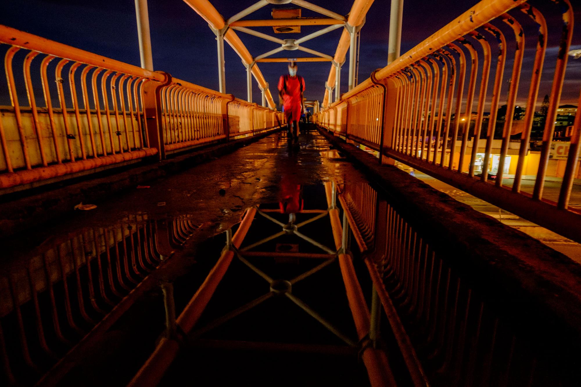 Un hombre camina sobre su reflejo en un charco de agua que se forma en el puente peatonal en el kilómetro 9 de la autopista Duarte, a pocas horas de iniciar el toque de queda. Foto: Ricardo Hernández / Diario Libre