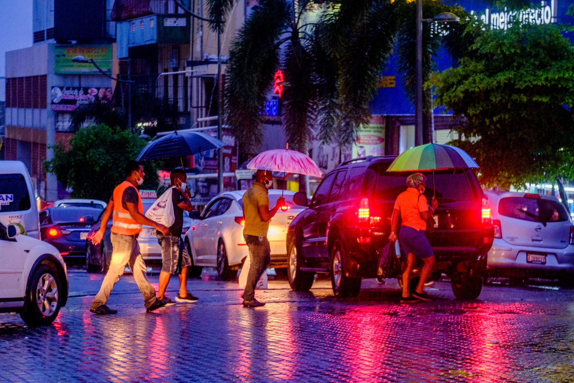 Varias mujeres y hombres cruzan la avenida Duarte en la esquina de la calle Ravelo de San Carlos, buscando transporte. Bajo lluvia las opciones de transporte se reducen y dificulta. 