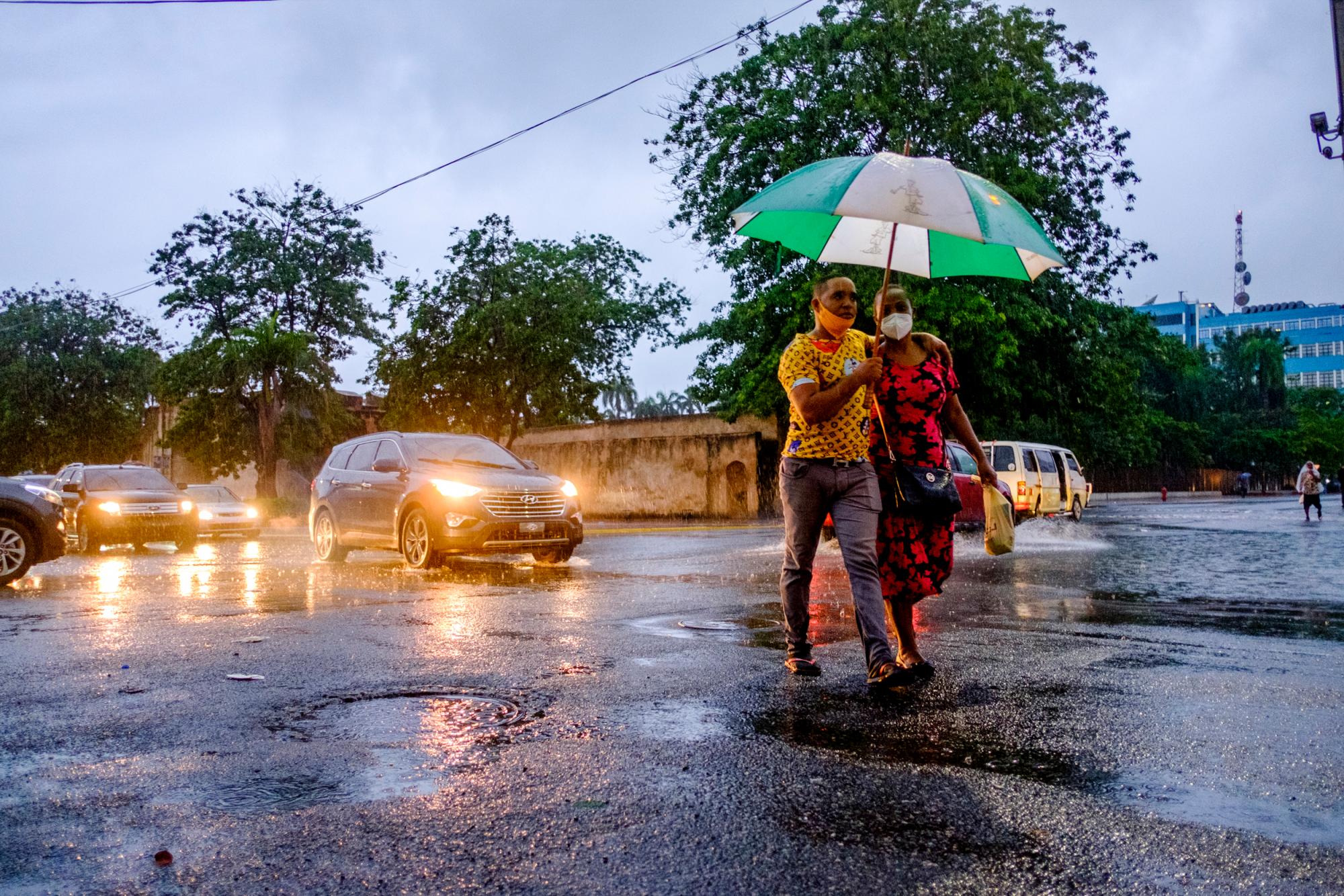 Una pareja camina por el medio de la vía, desafiando el tránsito por evitar un charco de agua que se forma en la calle Palo Hincado esquina avenida Bolívar de la Ciudad Colonial de Santo Domingo.